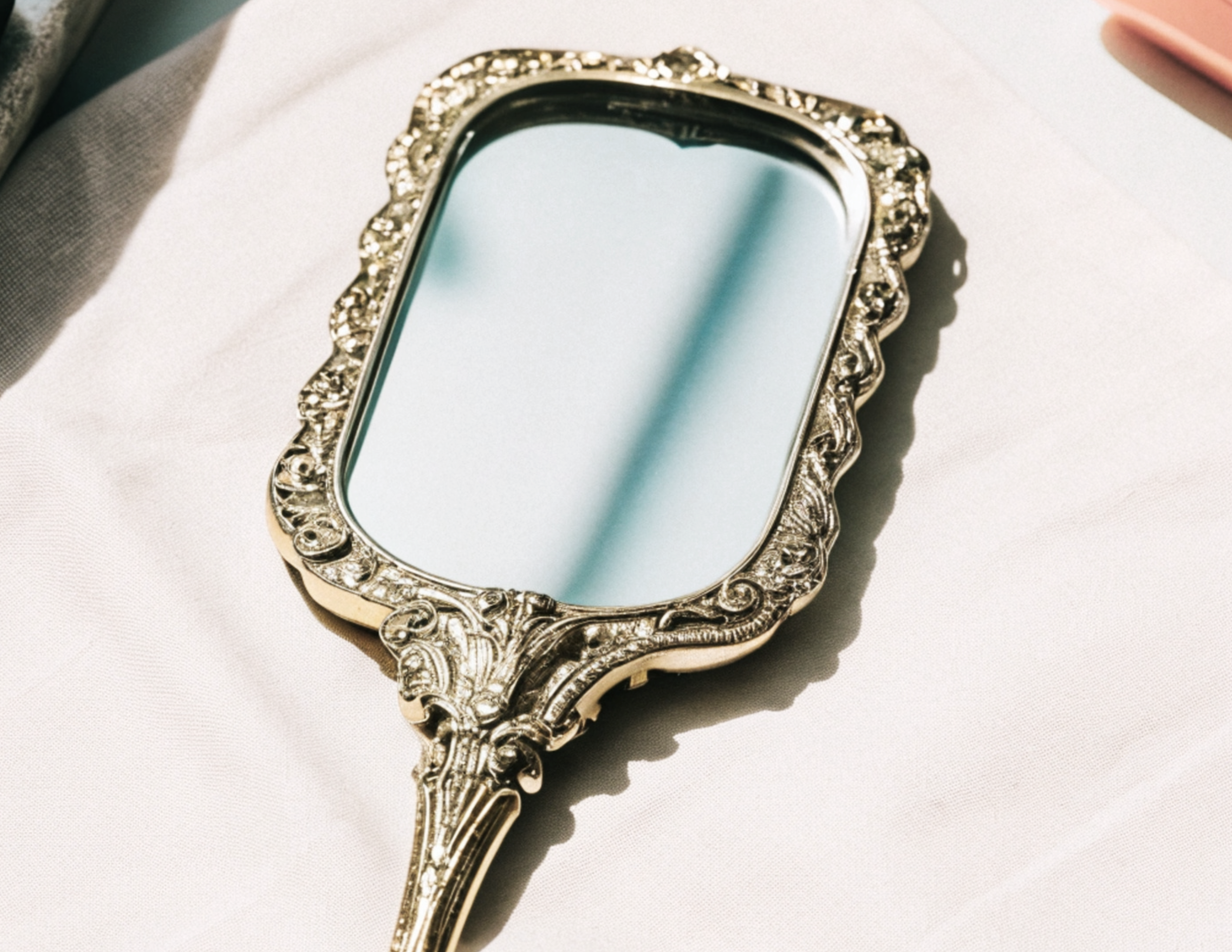 Ornate vintage hand mirror with a decorative silver frame resting on a white surface.