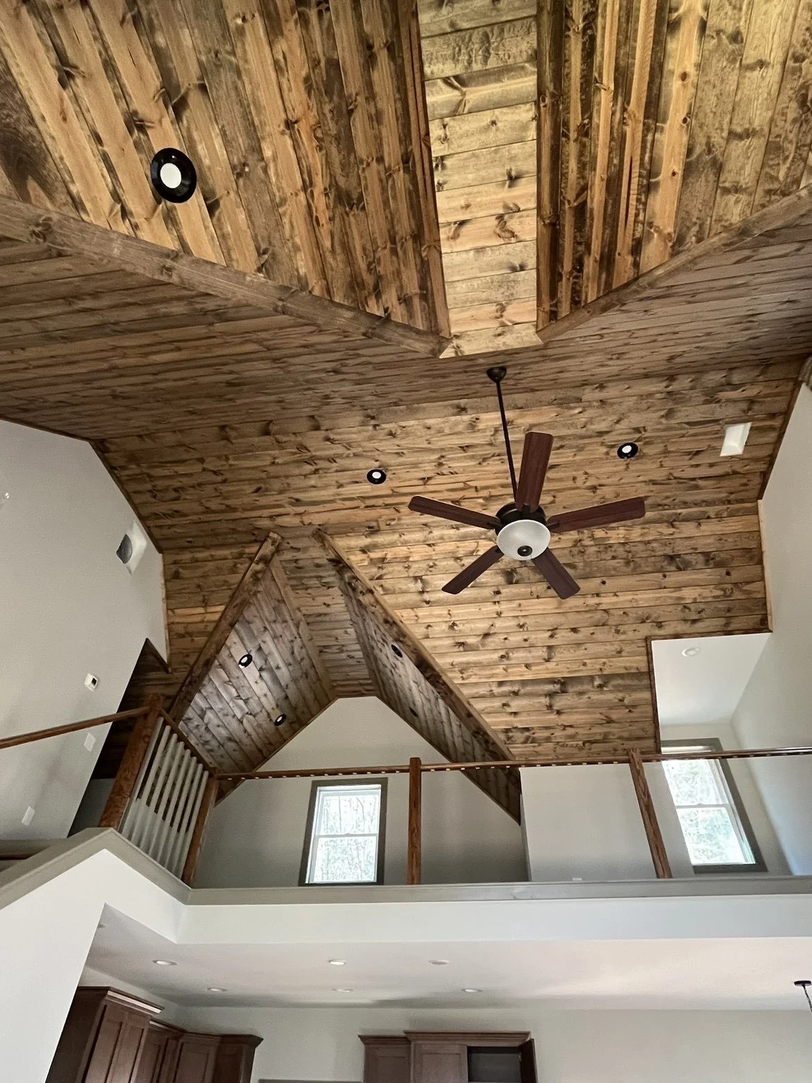 Interior view of a house with a high vaulted wooden ceiling, ceiling fan, and large windows letting in natural light.
