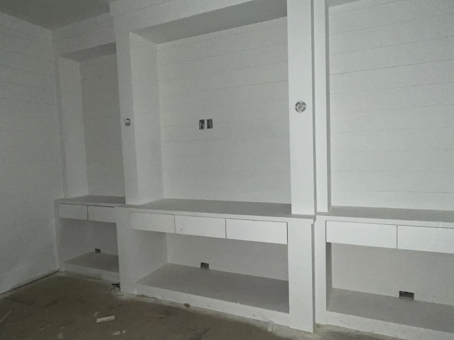 White built-in cabinets with shelves and drawers under construction in a room.