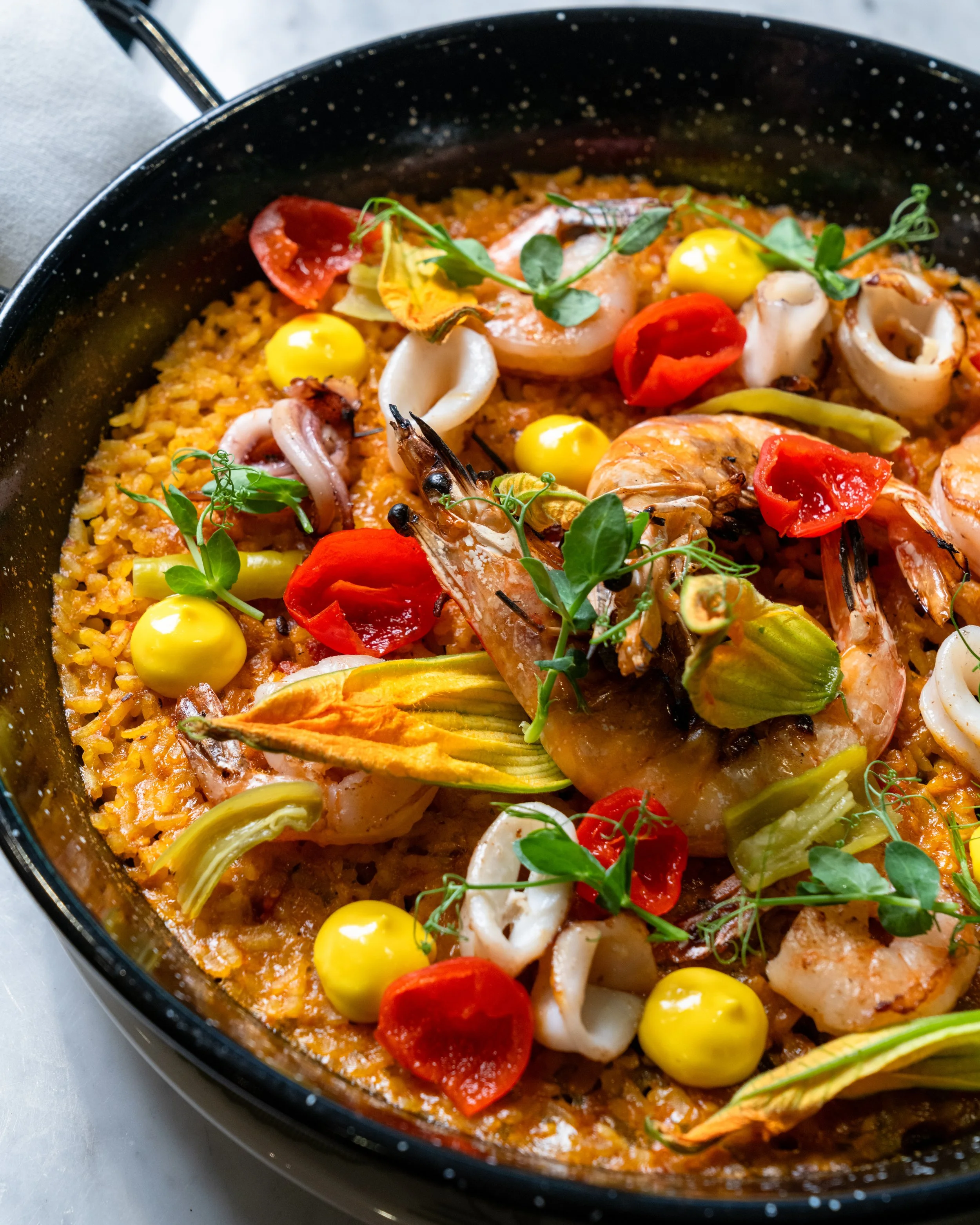 Dish of shrimp paella with rice, cherry tomatoes, herbs, and seafood, served in a black pan.