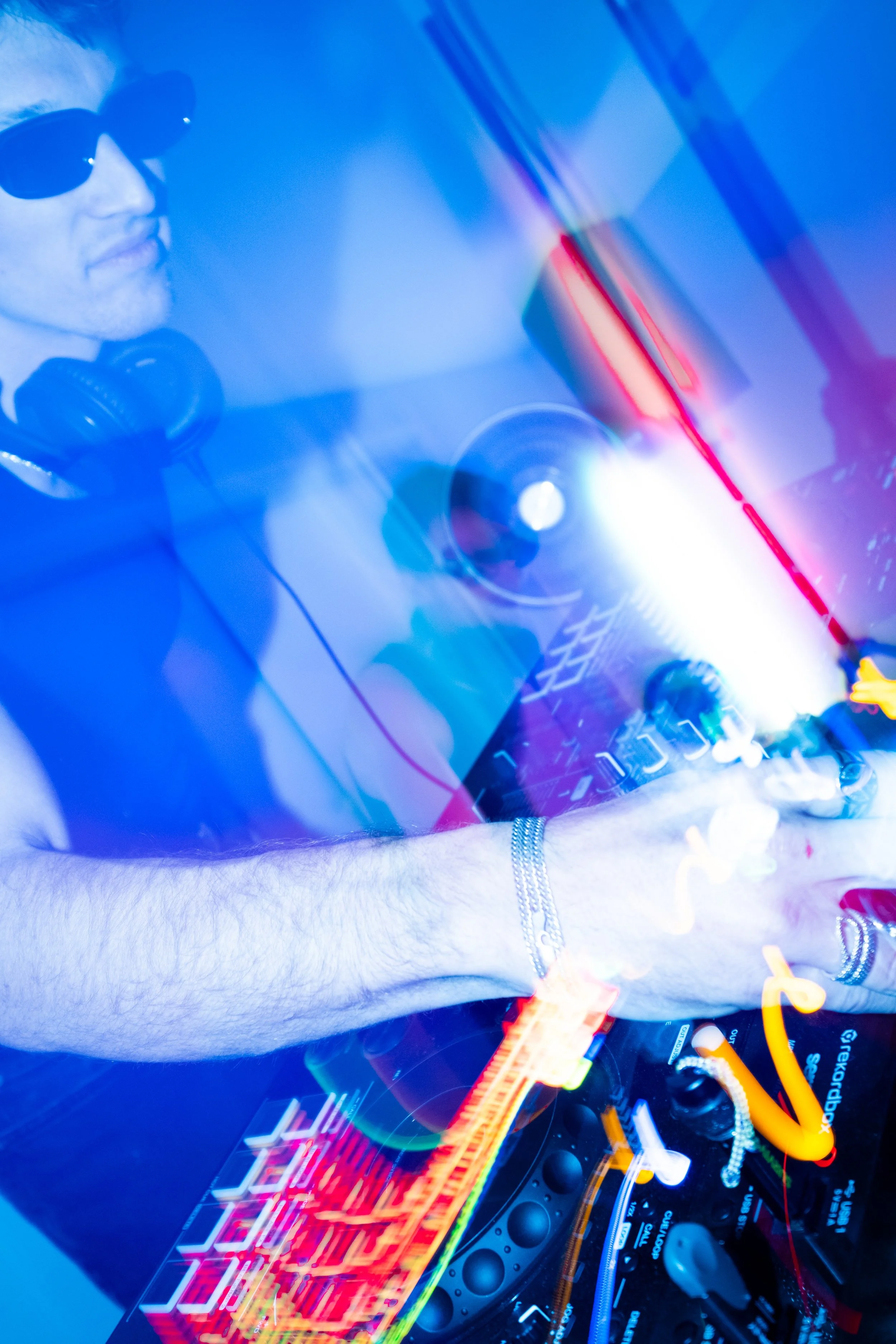 Close-up of a DJ with sunglasses and headphones, mixing music with colorful lights and digital music equipment.