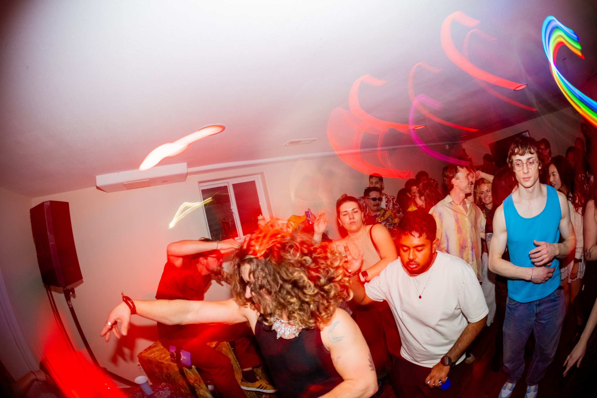 People dancing and socializing at a party with colorful lights and a lively atmosphere.