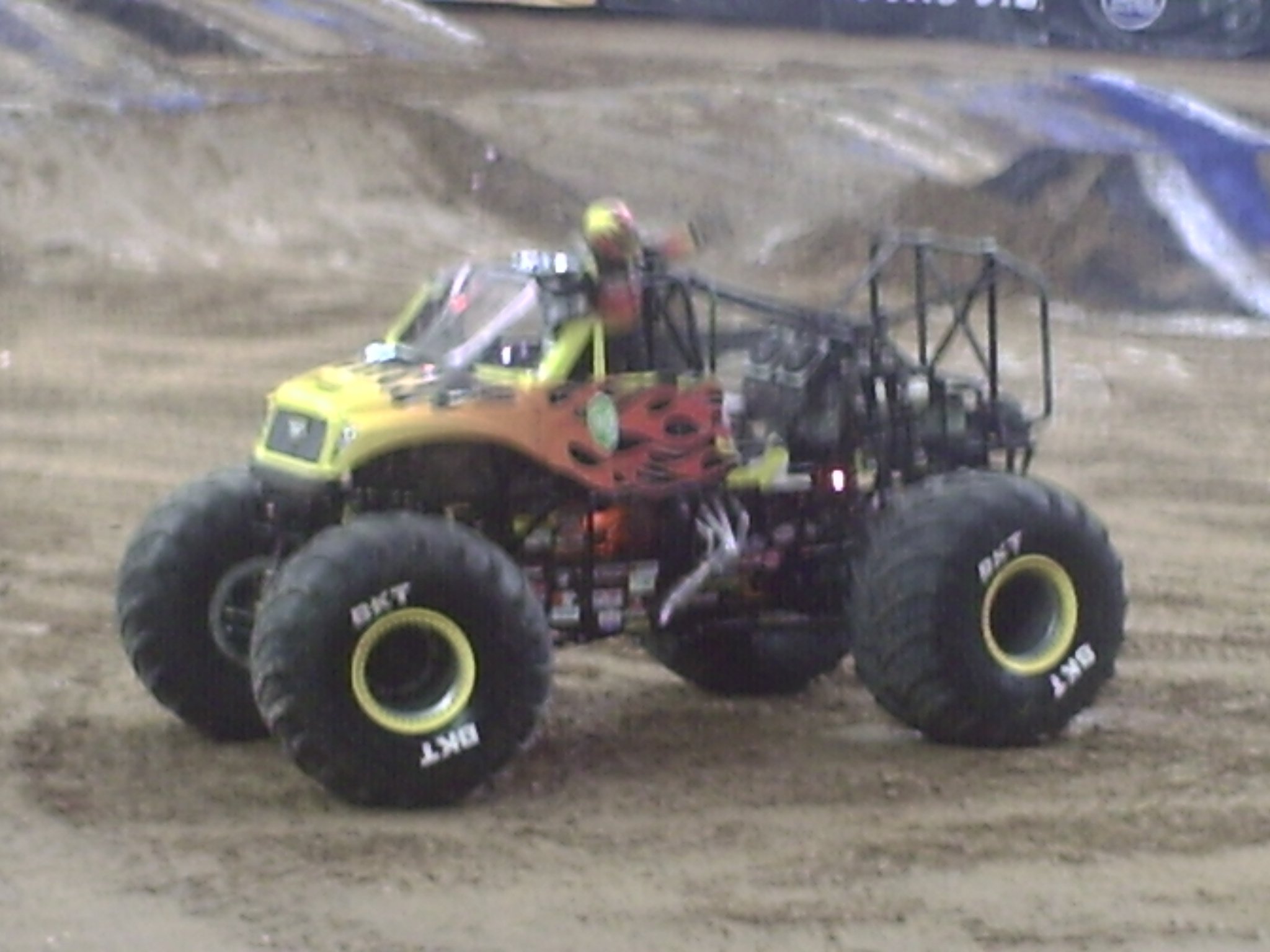 A bright yellow and black RC monster truck on a dirt track, with large tires and a detailed body.