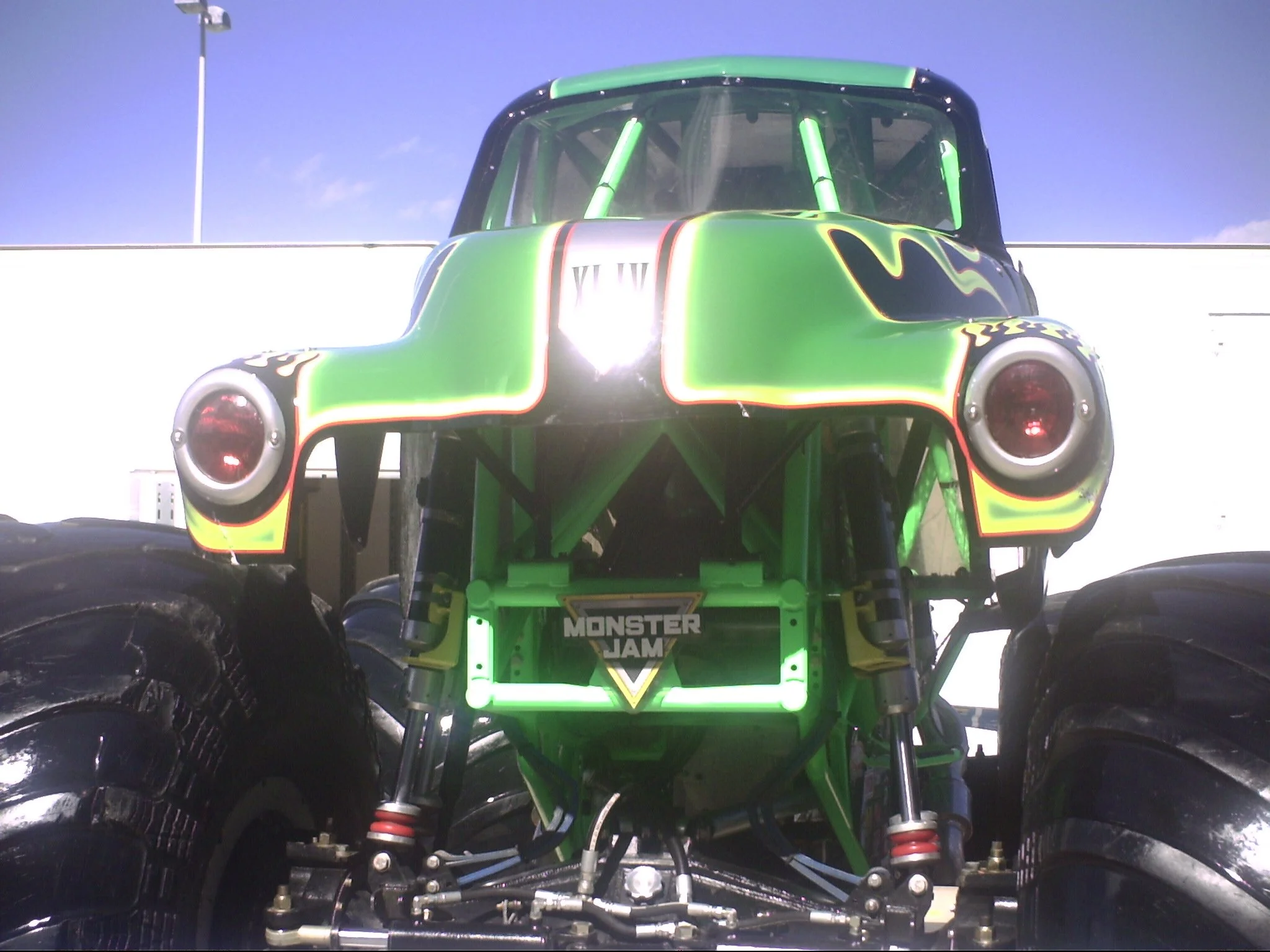 Colorful monster truck with neon green, black, red, and yellow accents, featuring large tires and a custom design, parked under a clear blue sky.