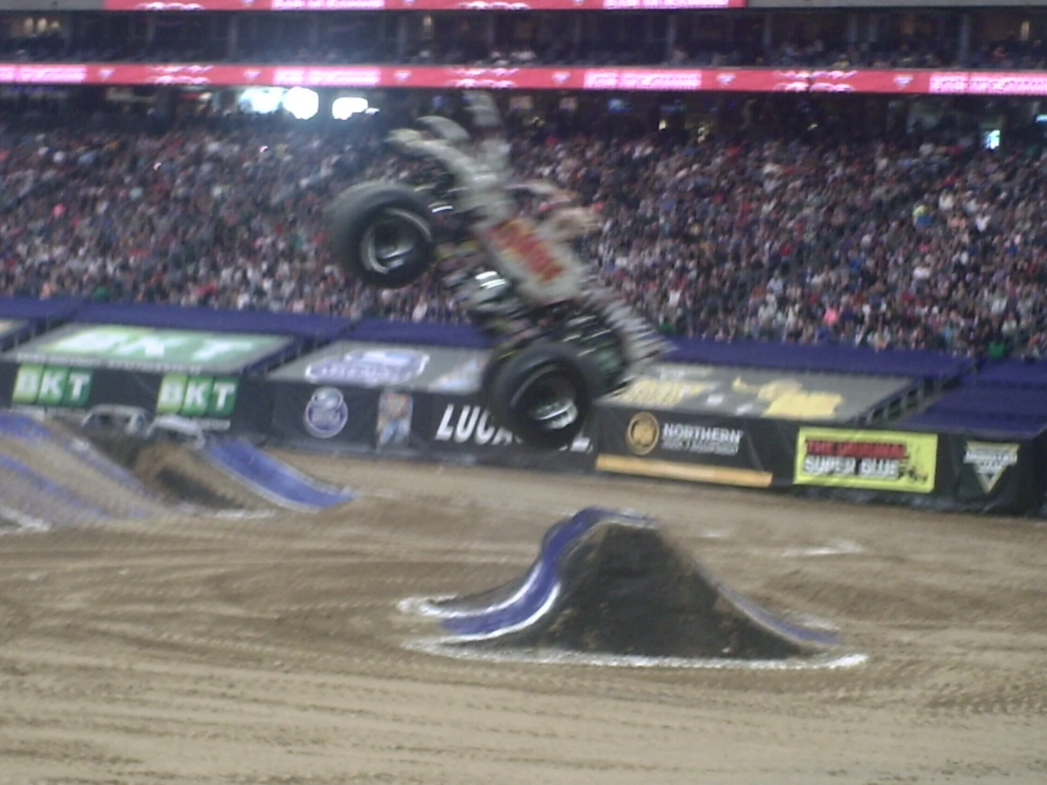 A monster truck in mid-air during a stunt at a packed stadium event.