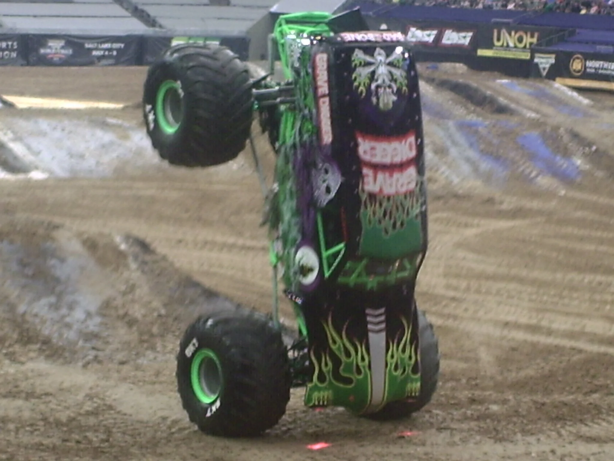 Side view of a monster truck on dirt track, black with green flame design, large tires, and detailed artwork.