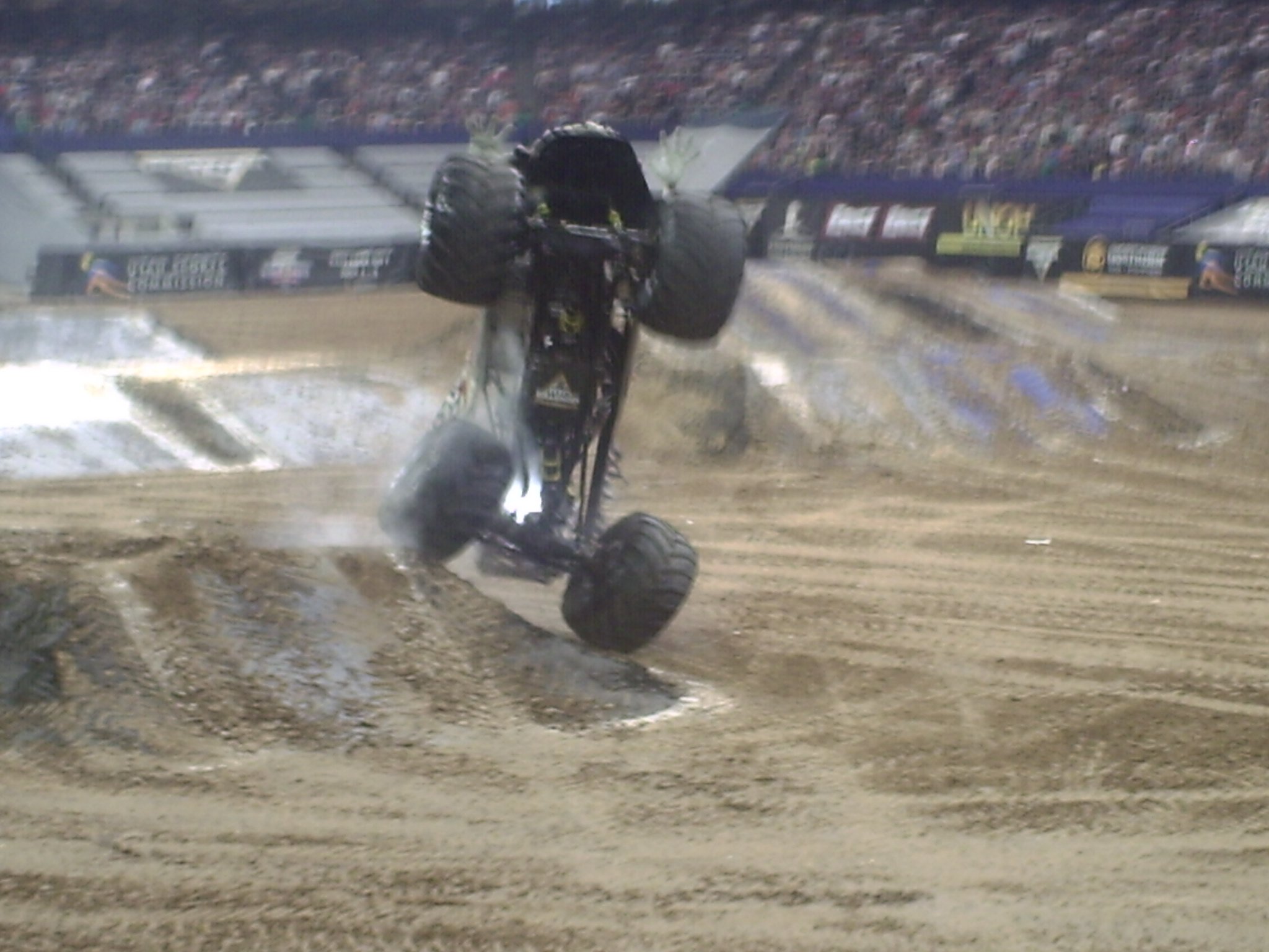 Motocross rider crashing during a race on a dirt track with a large crowd of spectators in the stadium.