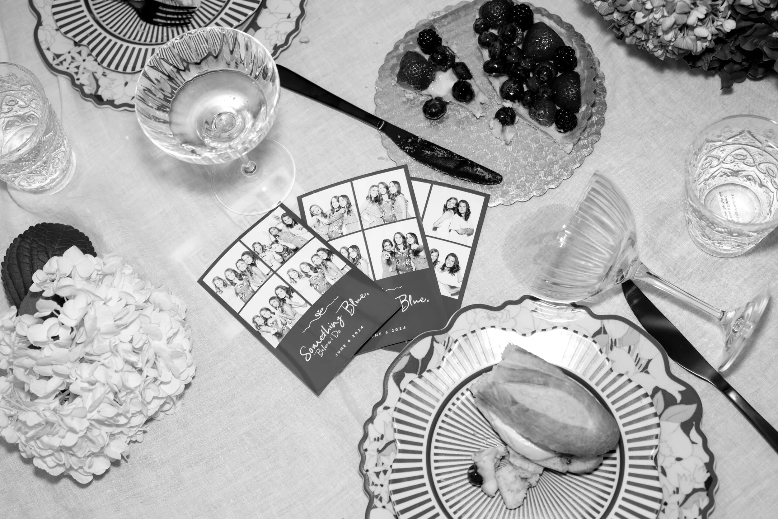 A table with a partially sliced berry tart, photo booth strips featuring a group of women, decorative plates, glassware, and floral arrangements.