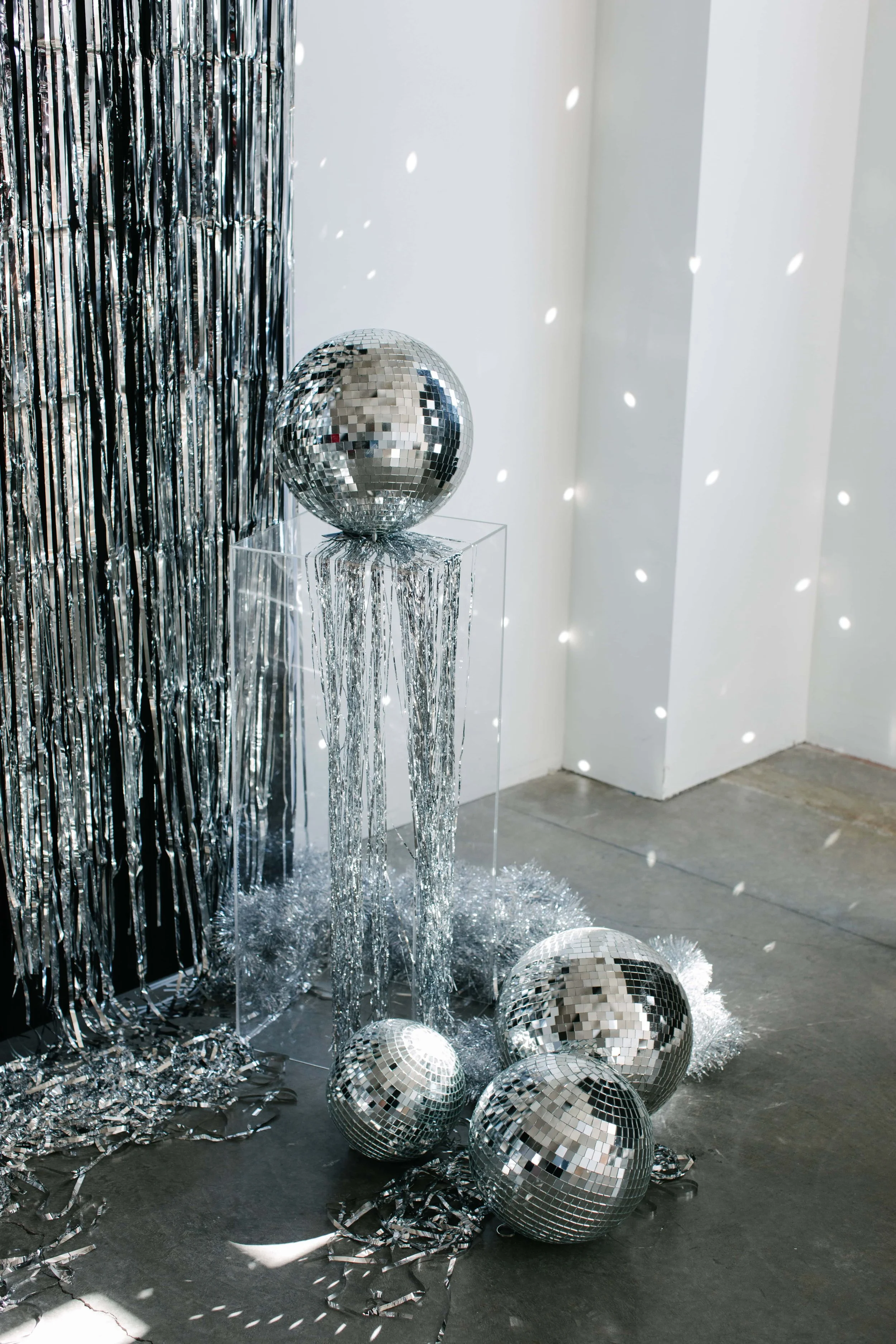 Disco balls and silver tinsel decorations on the floor, with a silver curtain in the background, creating a festive party or celebration scene.