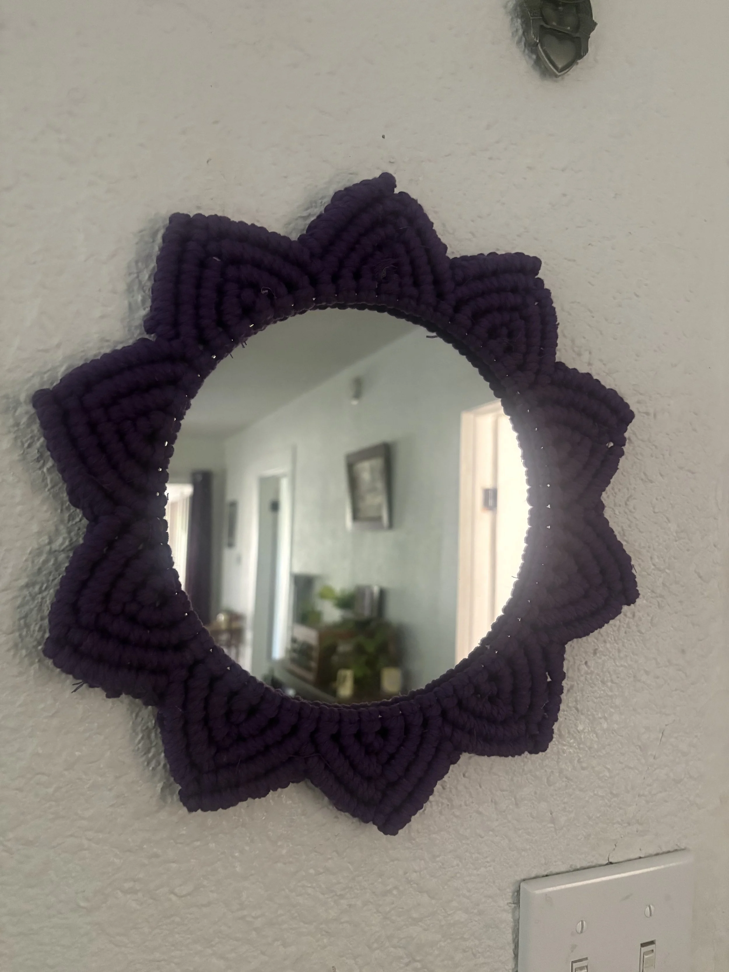 Midnight Bloom Mirror
(12" x 12")
A striking macramé mirror framed with layered petals in deep purple cord. Inspired by blooming flowers and celestial nights, this piece adds texture and drama to any space. 
$80.00