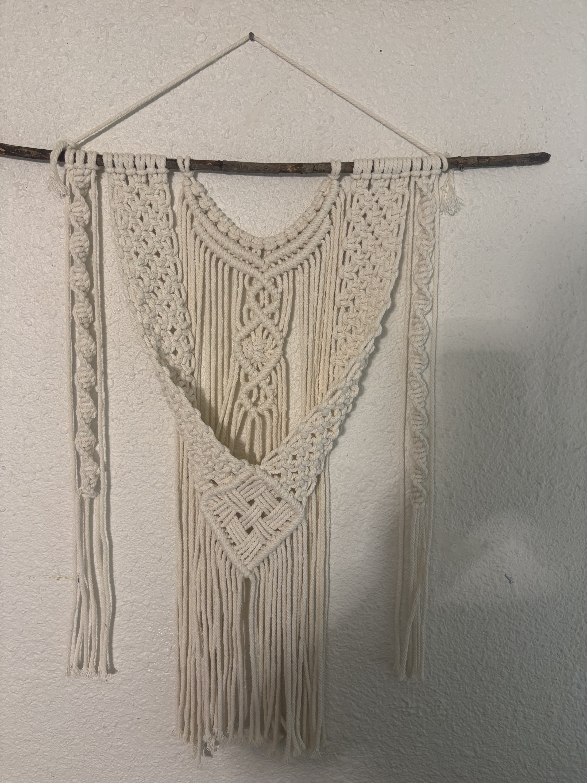 Woodland Weave
(16" x 25")
Intricate knotwork and layered textures come together in a flowing design inspired by forest paths and winding vines. Suspended from a natural branch, this statement piece brings warmth, movement, and organic charm to any s
