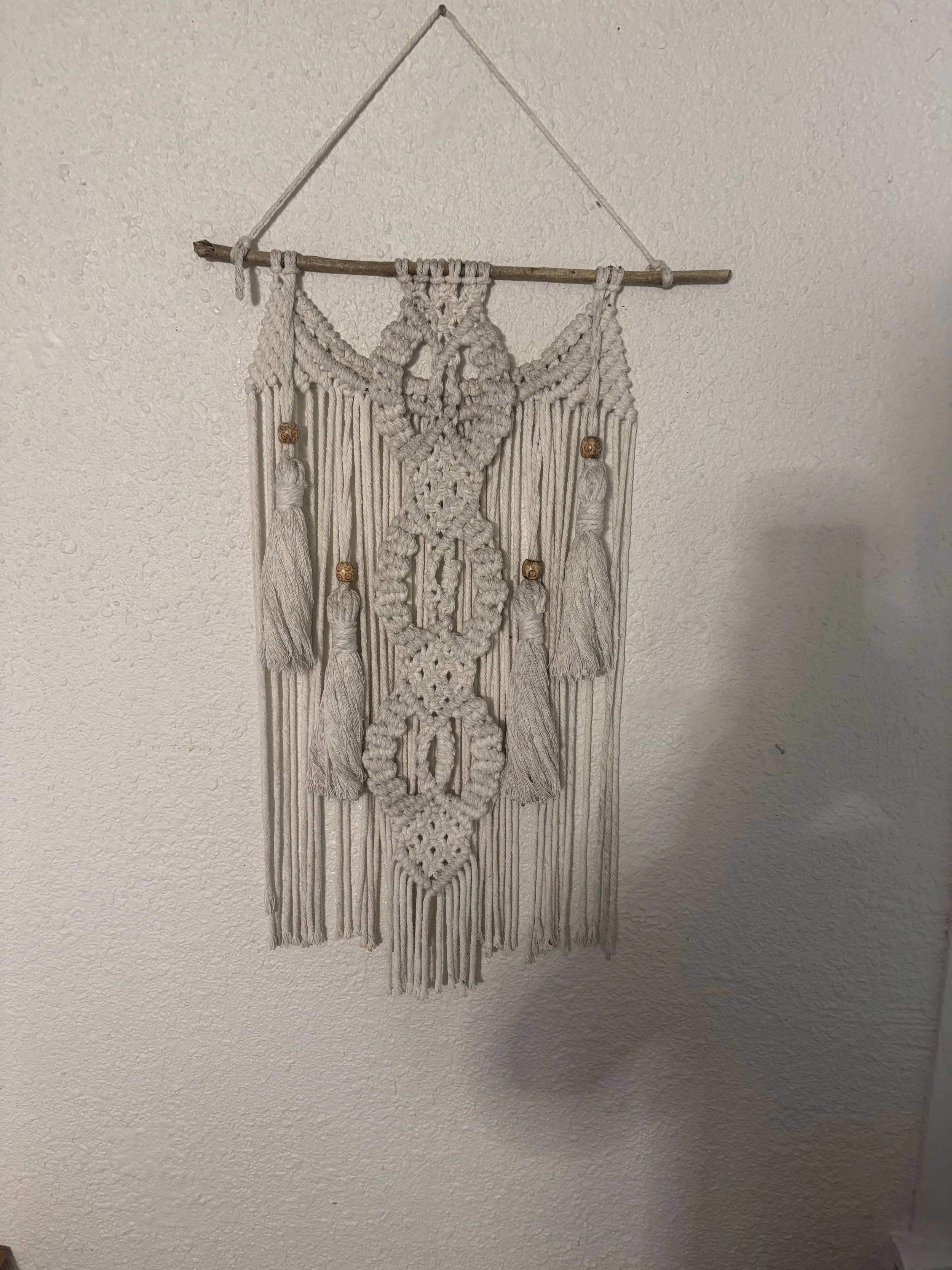 Spirit Weave
(13" x 25")
Intricate knotwork, layered textures, and decorative tassel accents come together in this eye-catching wall hanging. Suspended from a natural branch, this piece blends organic materials with detailed craftsmanship to create a
