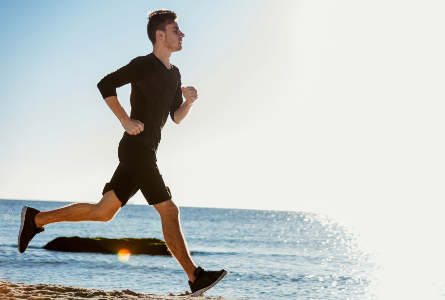 Man running beside the ocean as part of an active wellness routine