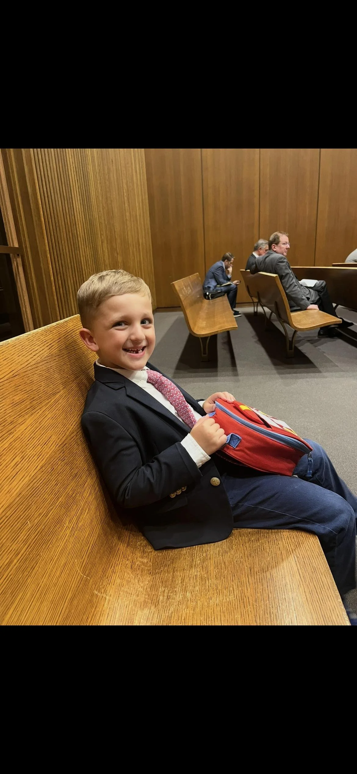 William Kopsick, dressed for court, sitting on a courtroom bench.