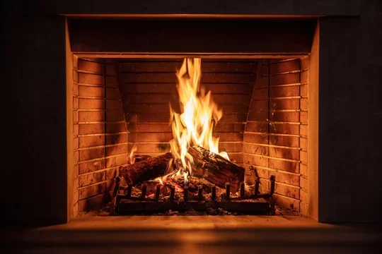 A lit fireplace with burning logs inside a brick hearth.