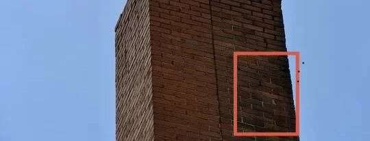 Close-up of a brick chimney with a red outline highlighting a section of the bricks against a blue sky.