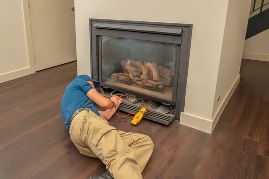A person lying on the floor repairing a direct vent gas fireplace.