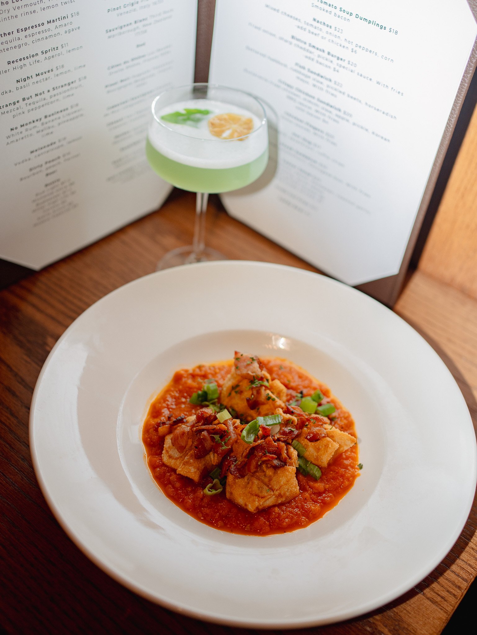 A white bowl of ravioli pasta with tomato sauce and chopped green onions, on a wooden table.