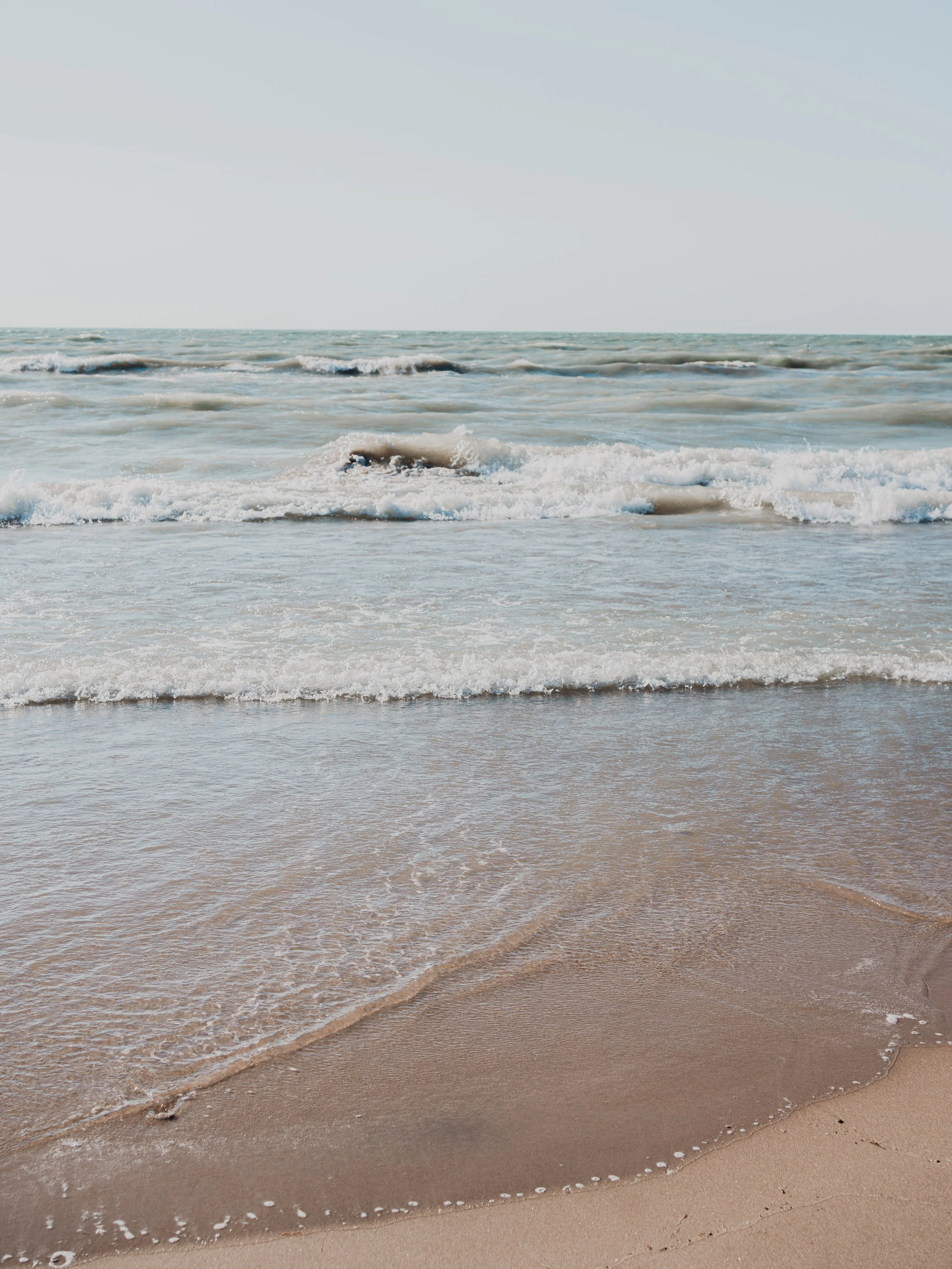 Calm ocean waves gently lapping onto a sandy shore under a clear sky.