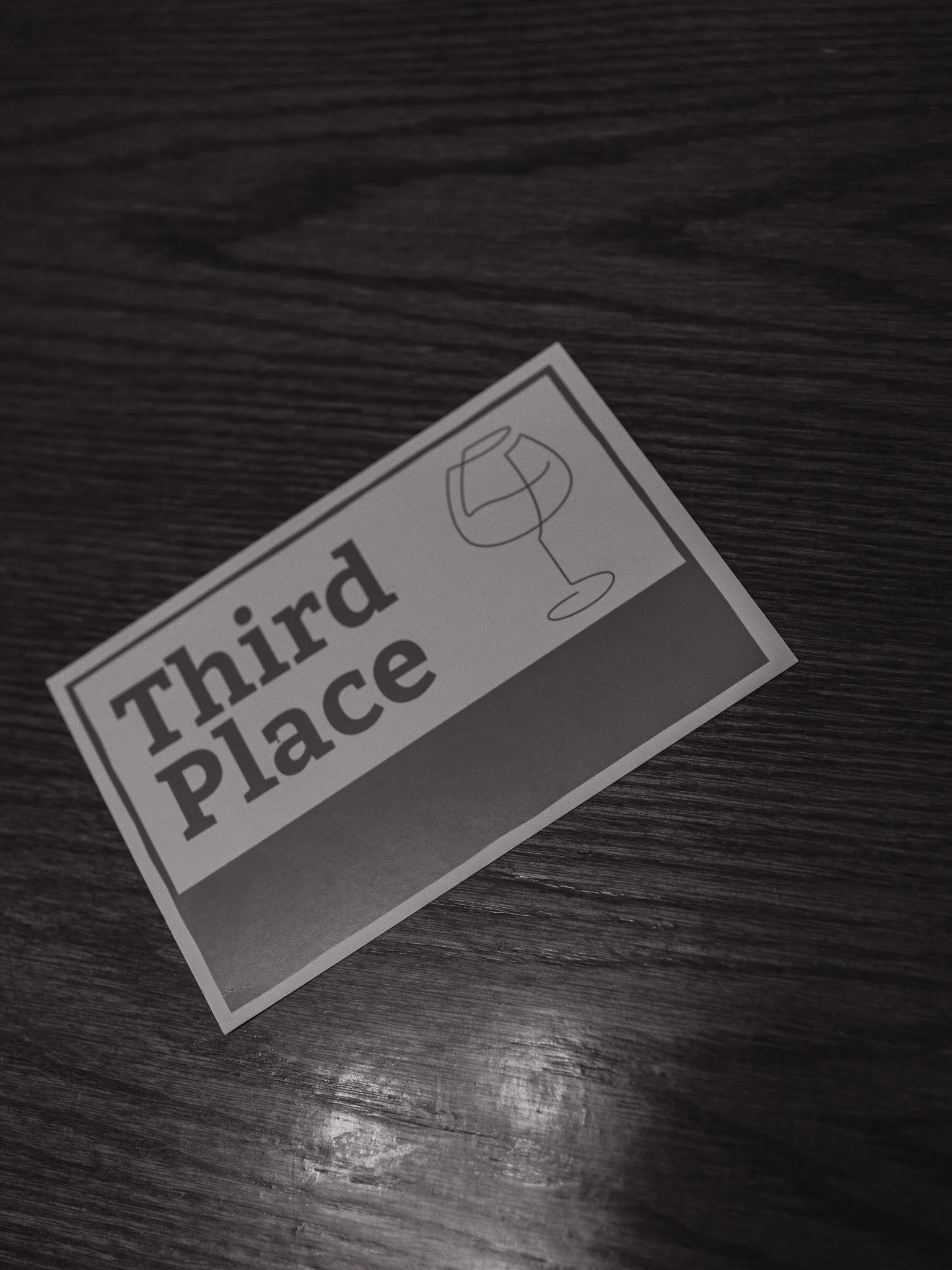 A close-up of a warning label on a dark wooden surface. The label has a hazard symbol indicating a harmful substance and the partially visible words 'Third place'.