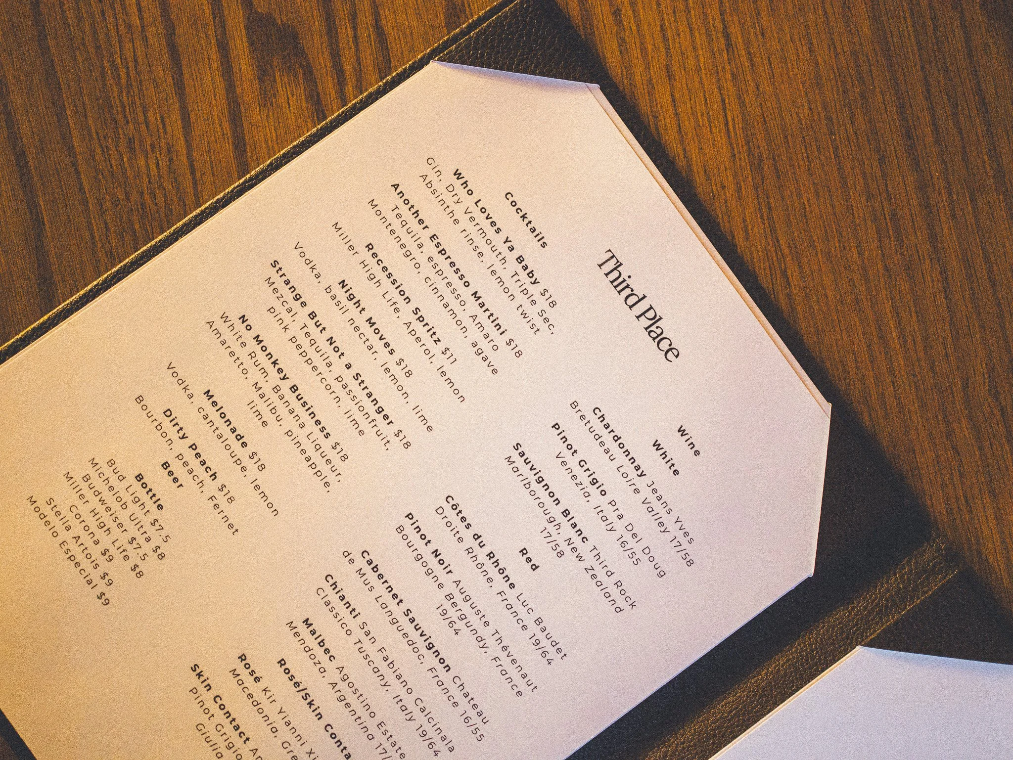 A menu titled 'Third Place' placed on a dark wood surface, with partial view of the menu showing drink options and descriptions.