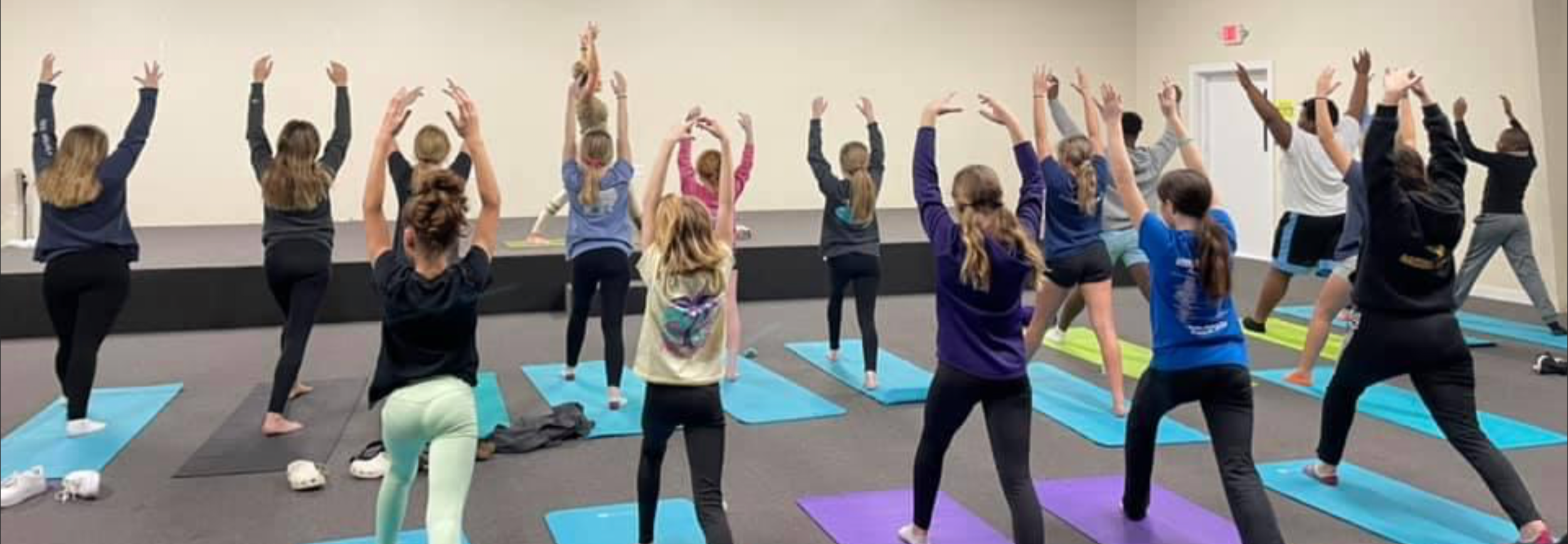 A group of young girls participating in a yoga class, practicing poses on colorful mats in a room with plain white walls.