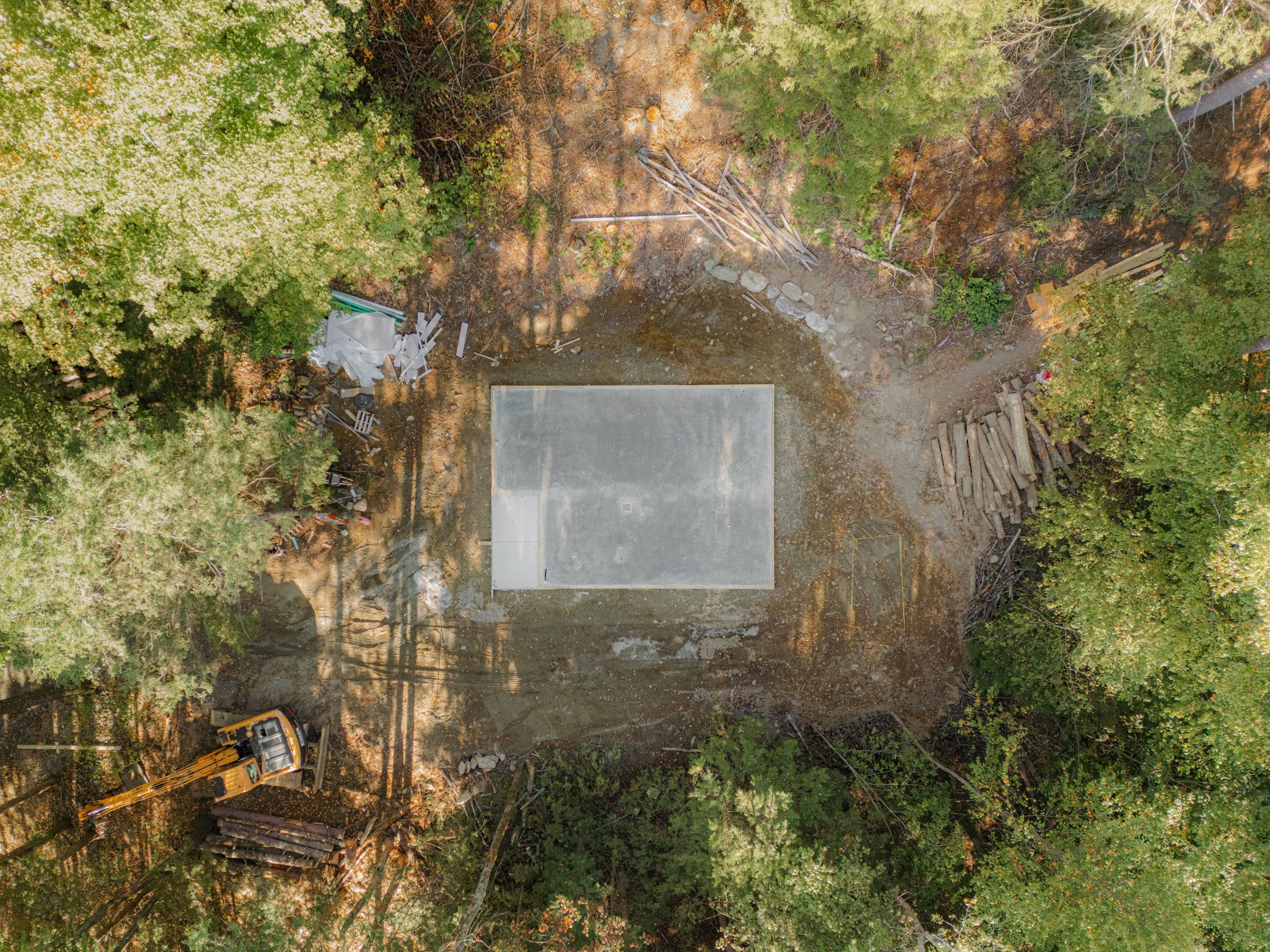 Aerial view of a construction site in a forest area with trees surrounding a cleared section of land, construction materials, and construction equipment.