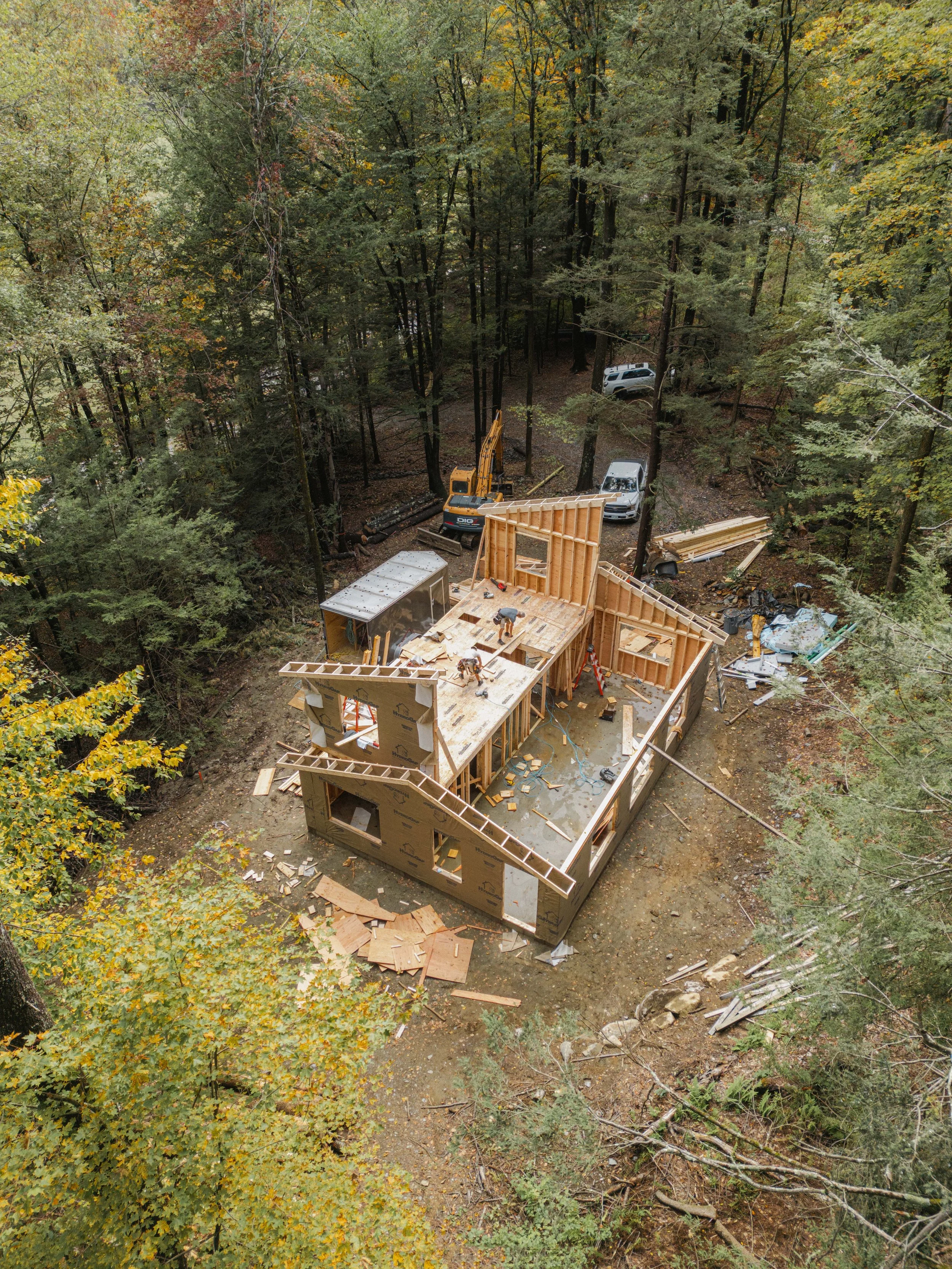 A bird's-eye view of a house under construction in a wooded area with trees and construction vehicles nearby.