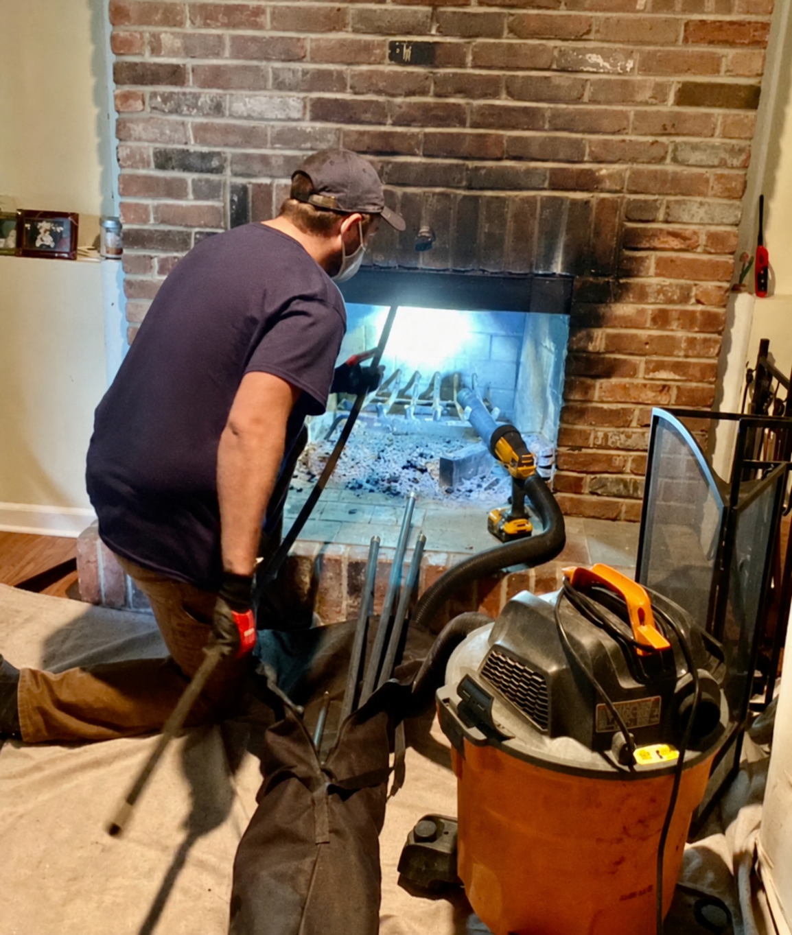 A person kneeling near a fireplace undergoing chimney cleaning or repair, with tools and equipment around. Two River Chimney Services serving Monmouth and Ocean County, NJ