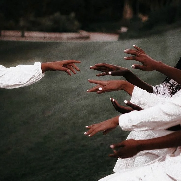 Multiple people reaching their hands toward each other outdoors during evening.
