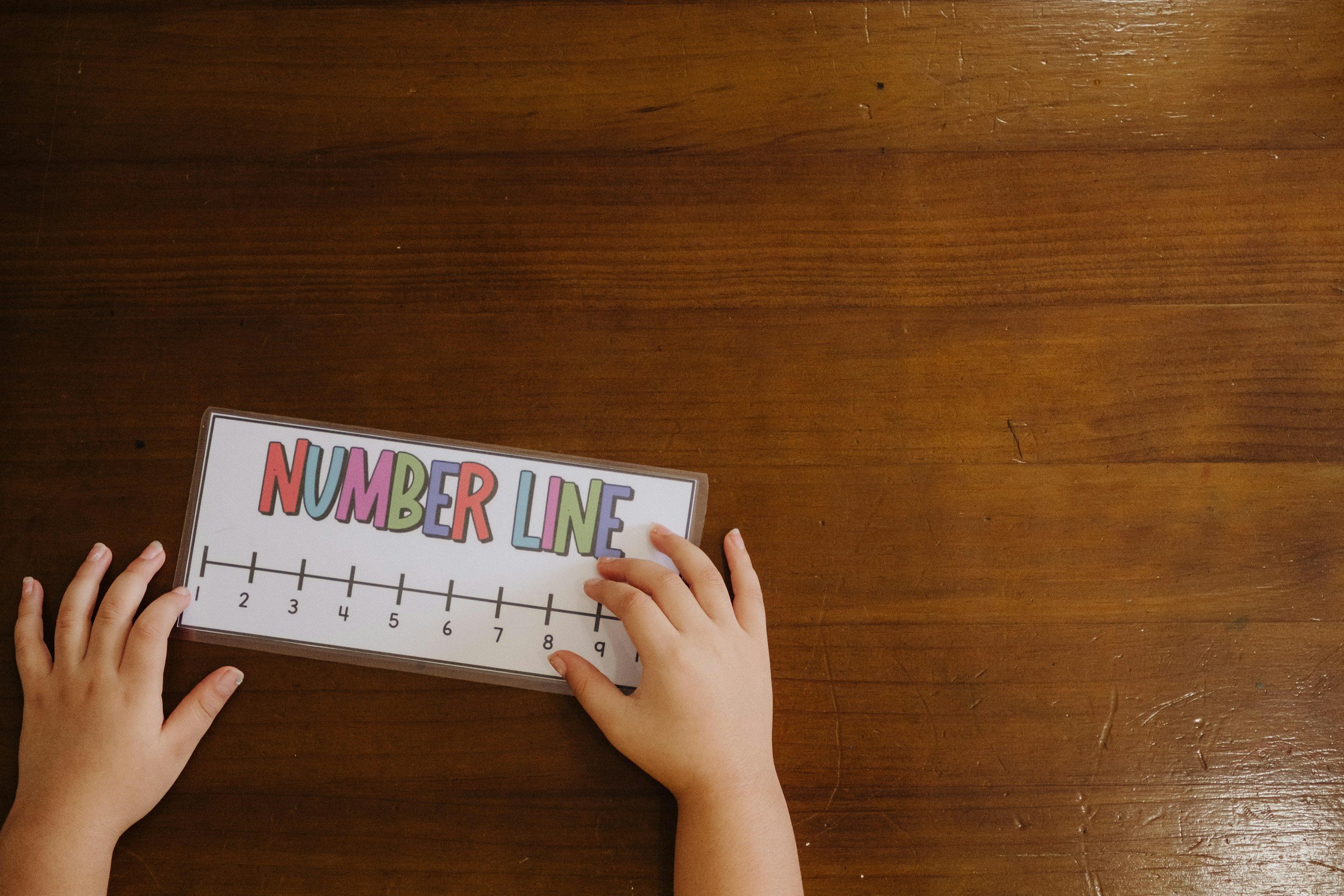 Childrens hands holding a number line educational chart on a wooden table.