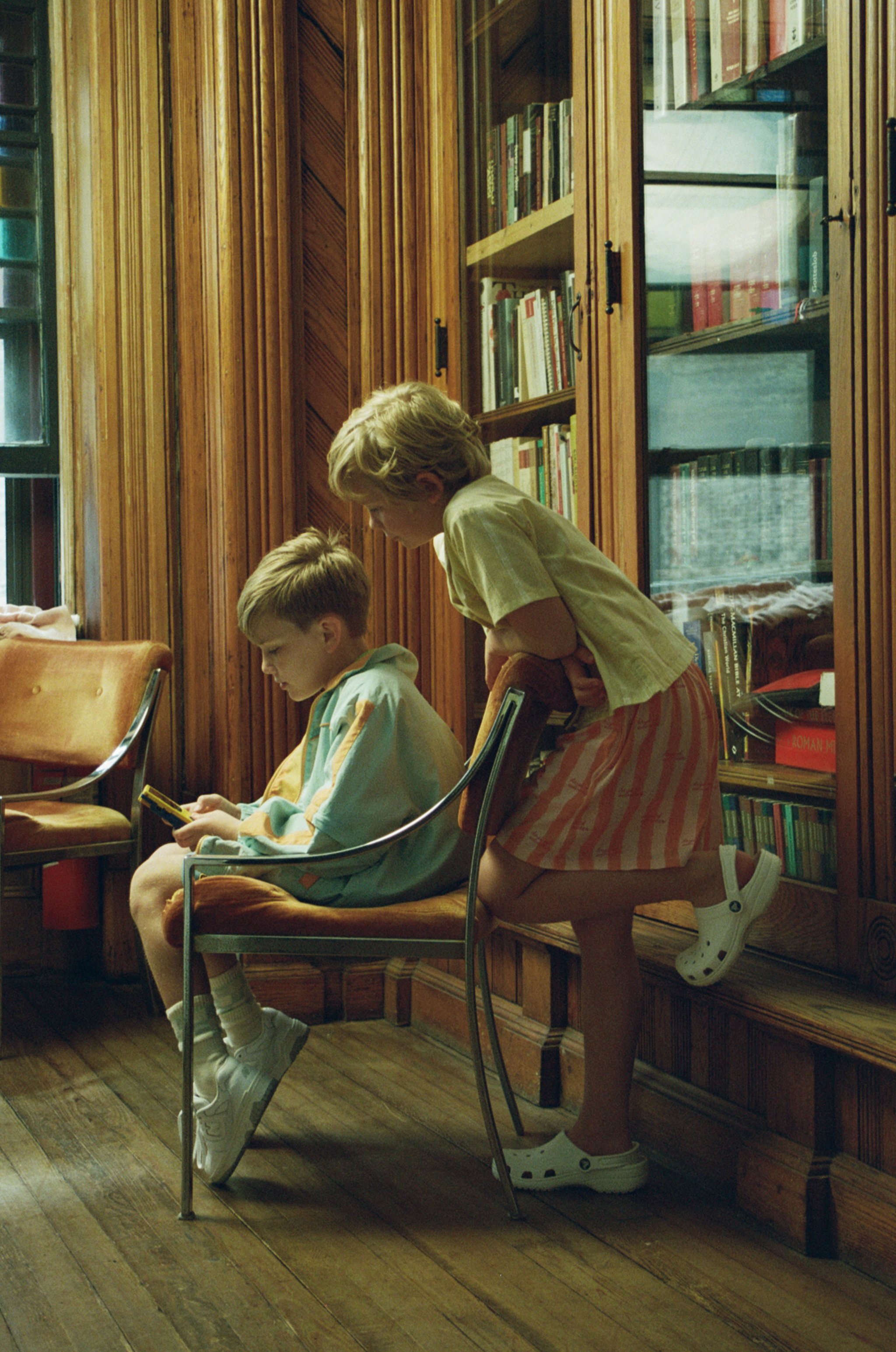 A woman bending over a seated child in a room with wood-paneled walls and bookshelves filled with books.