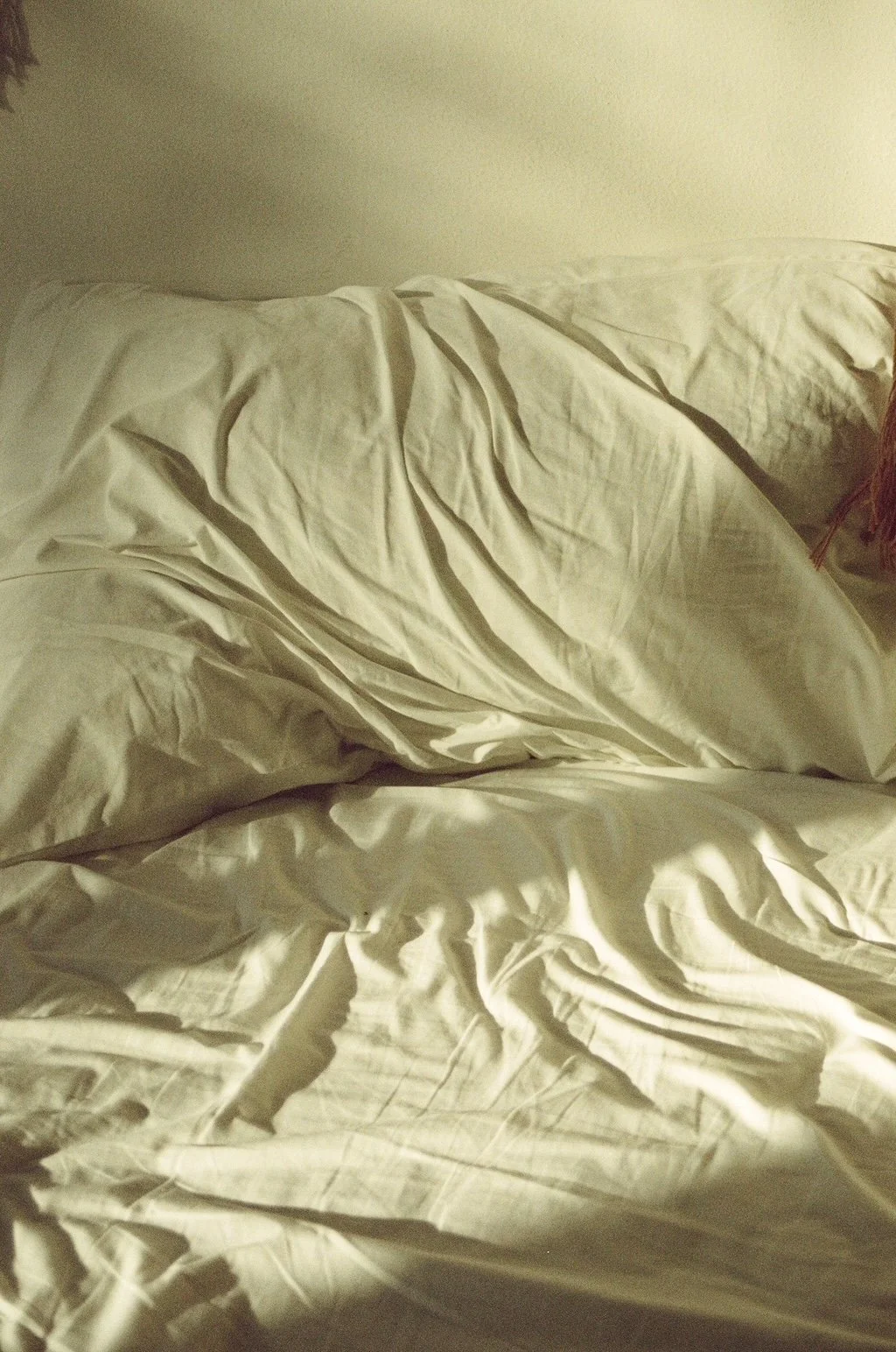 Unmade bed with white sheets and pillows, slightly wrinkled and disheveled.