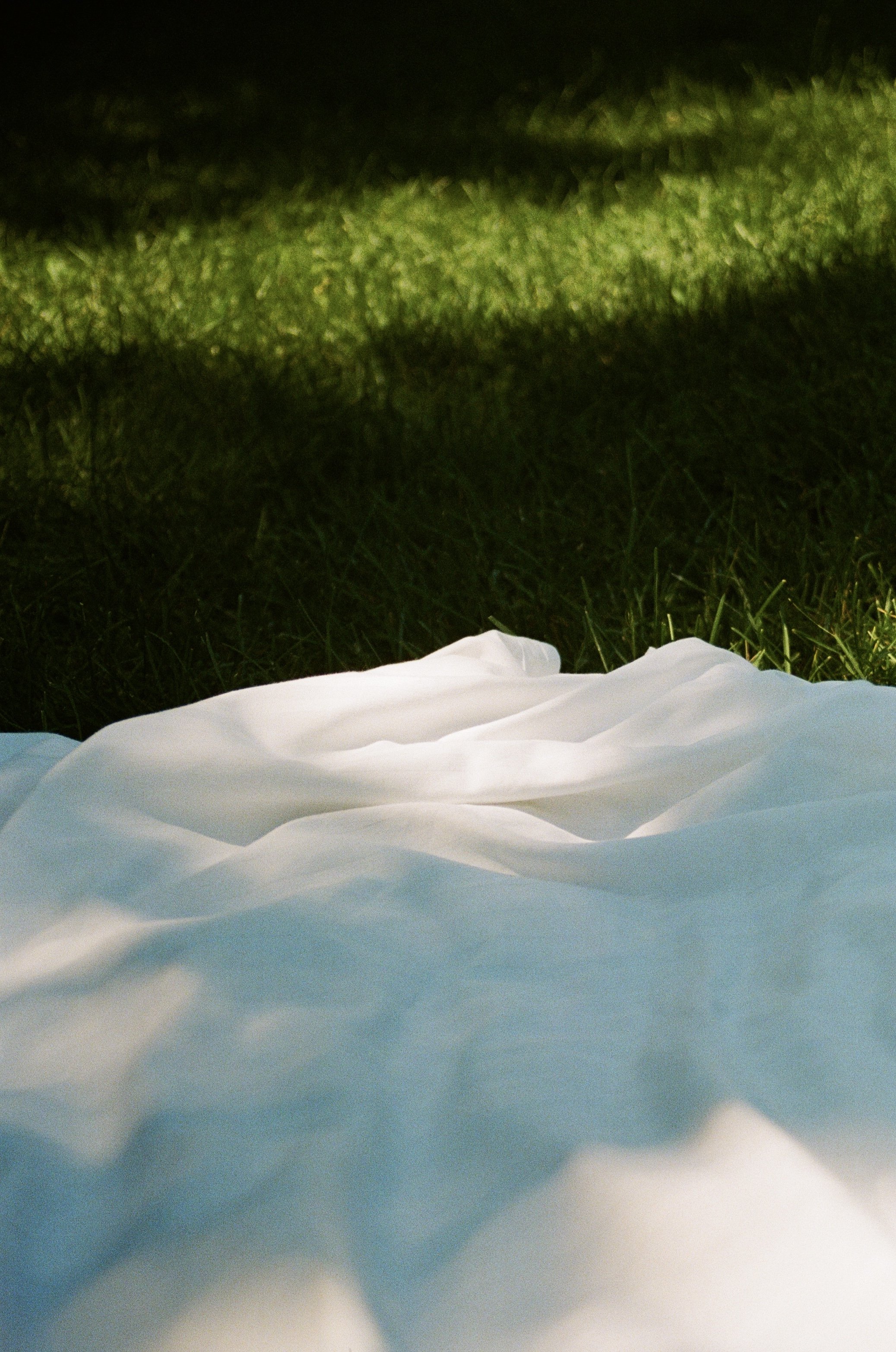 Close-up of a white fabric sheet on grass with green shadowed area in the background at night.