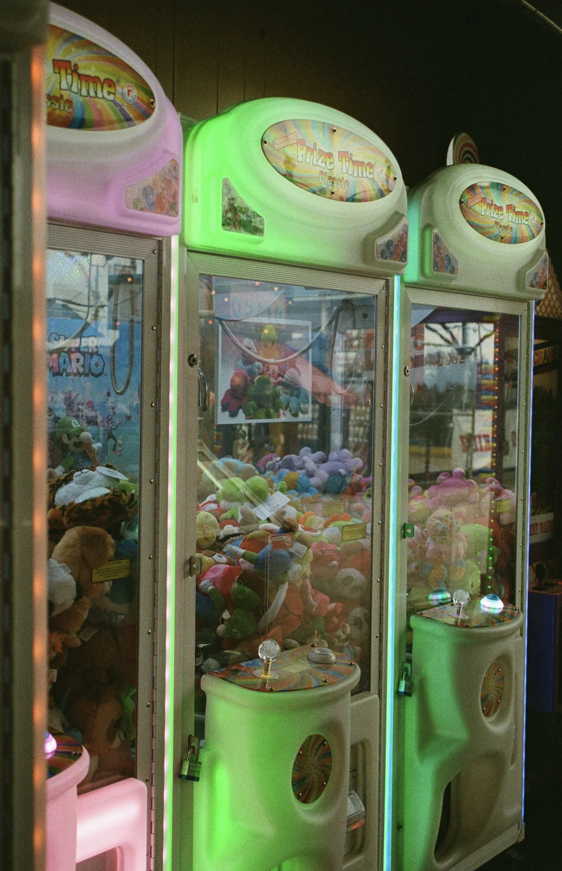 A row of three plush toy claw machines with colorful neon lights, filled with stuffed animals and toys inside at an arcade.