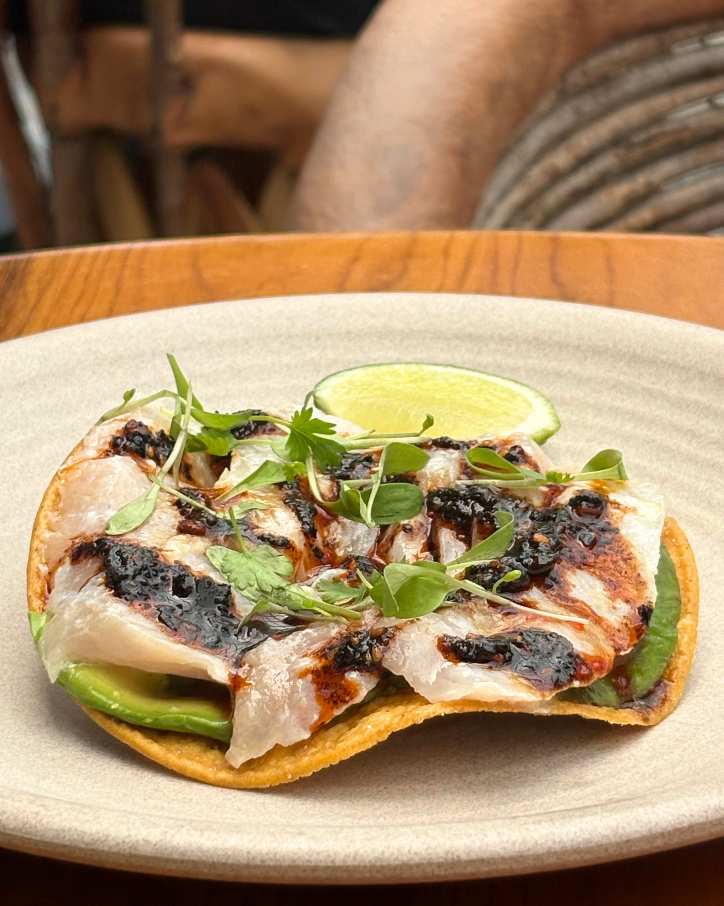 Close-up of a toasted sandwich with melted cheese, fresh green herbs, and a lime wedge on a beige ceramic plate.