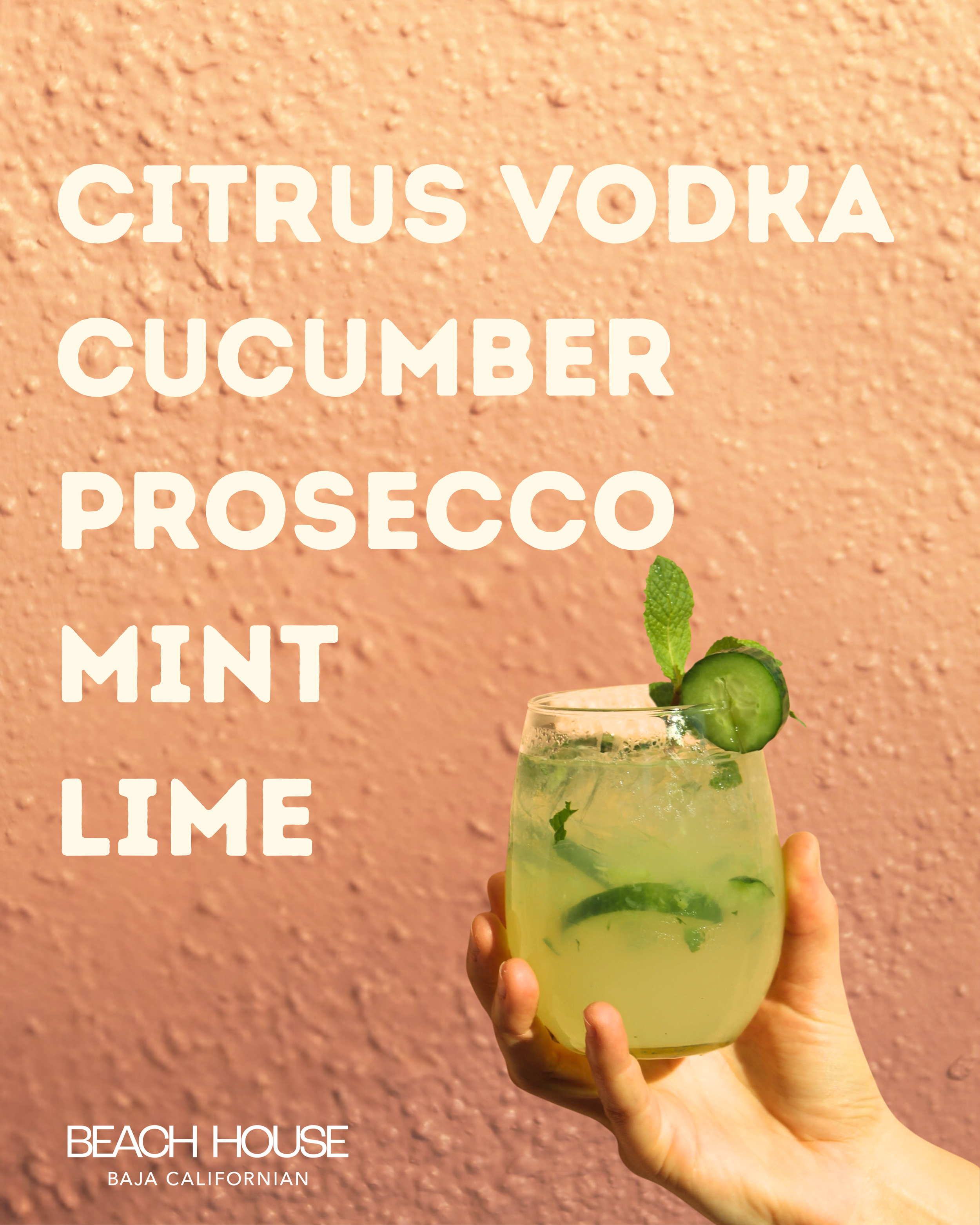 A hand holding a glass of lime and cucumber infused cocktail with mint garnished on top against a pink textured background with white text overlay listing drink ingredients: citrus vodka, cucumber, prosecco, mint, lime. Part of a sign for Beach House