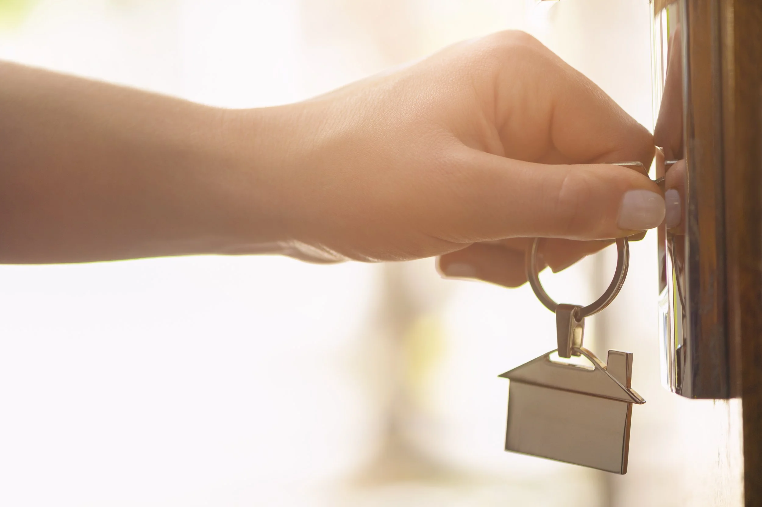 Close-up of a hand unlocking a door with a key, with a keychain attached, in front of a wooden door.