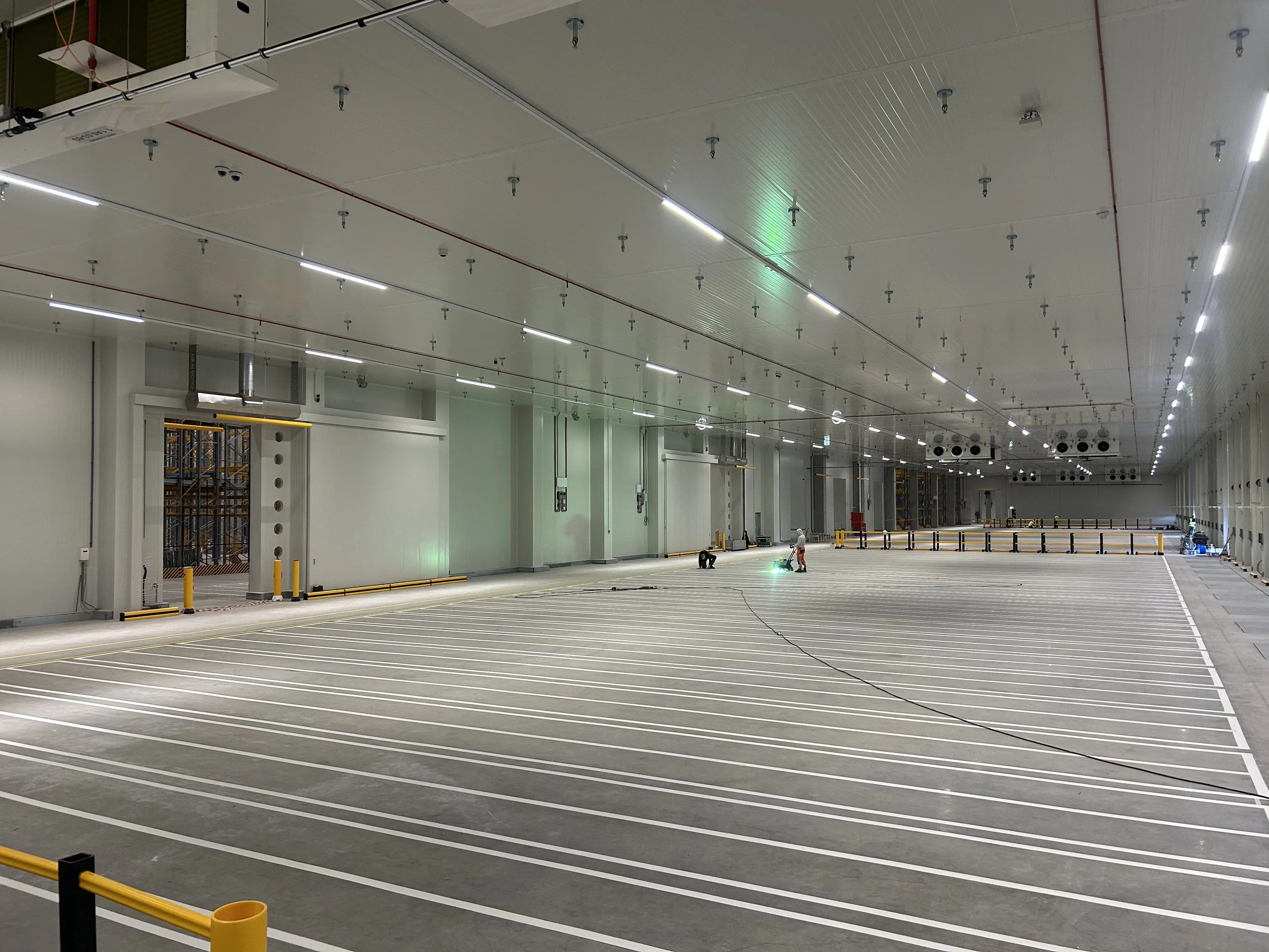 Grote, lege parkeergarage met wit plafond, verlichting, en enkele mensen die werkzaamheden uitvoeren.