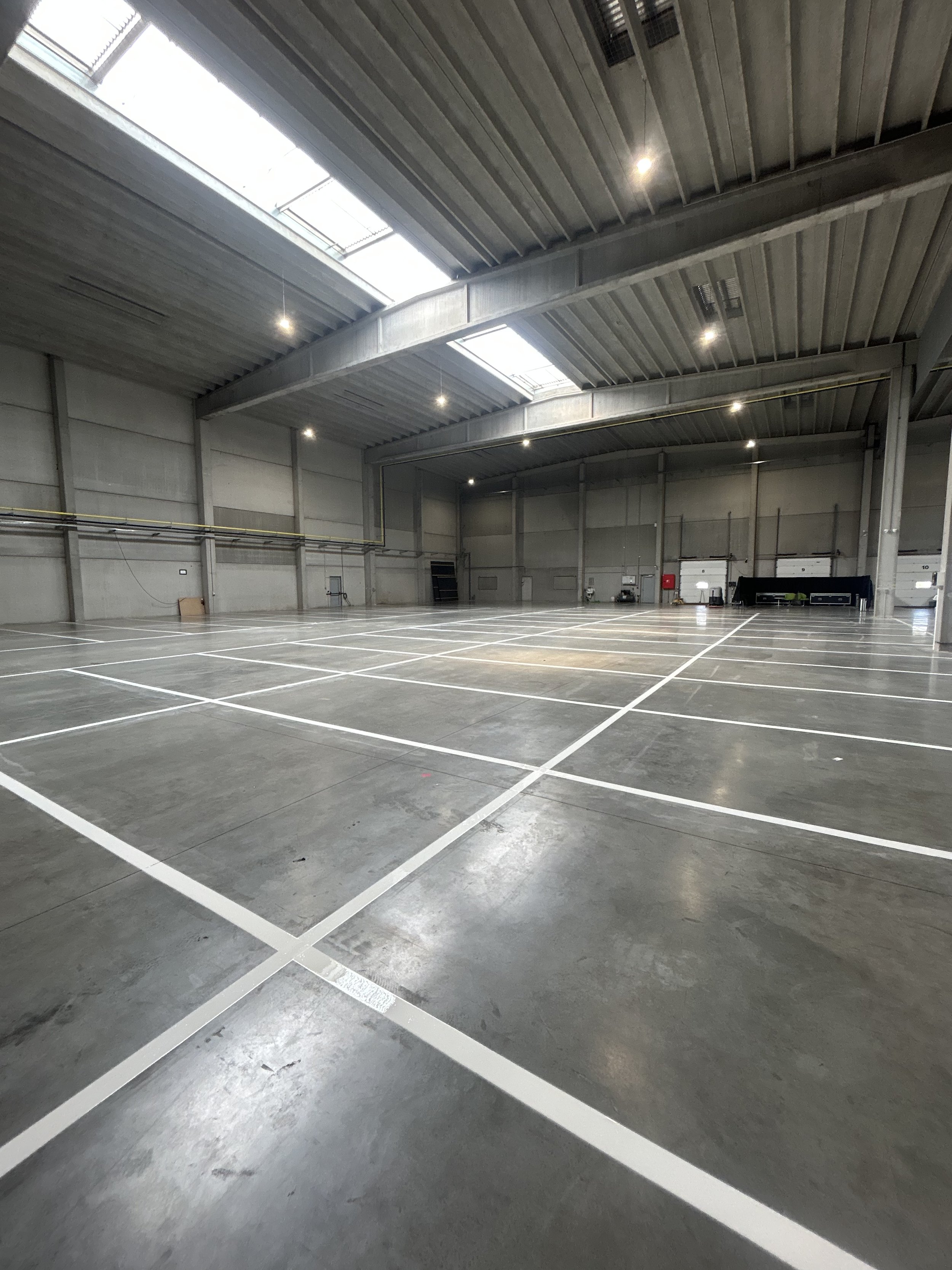 Een lege indoor sporthal met gestreepte lichtgrijze vloer en witte lijnen voor sportvelden.