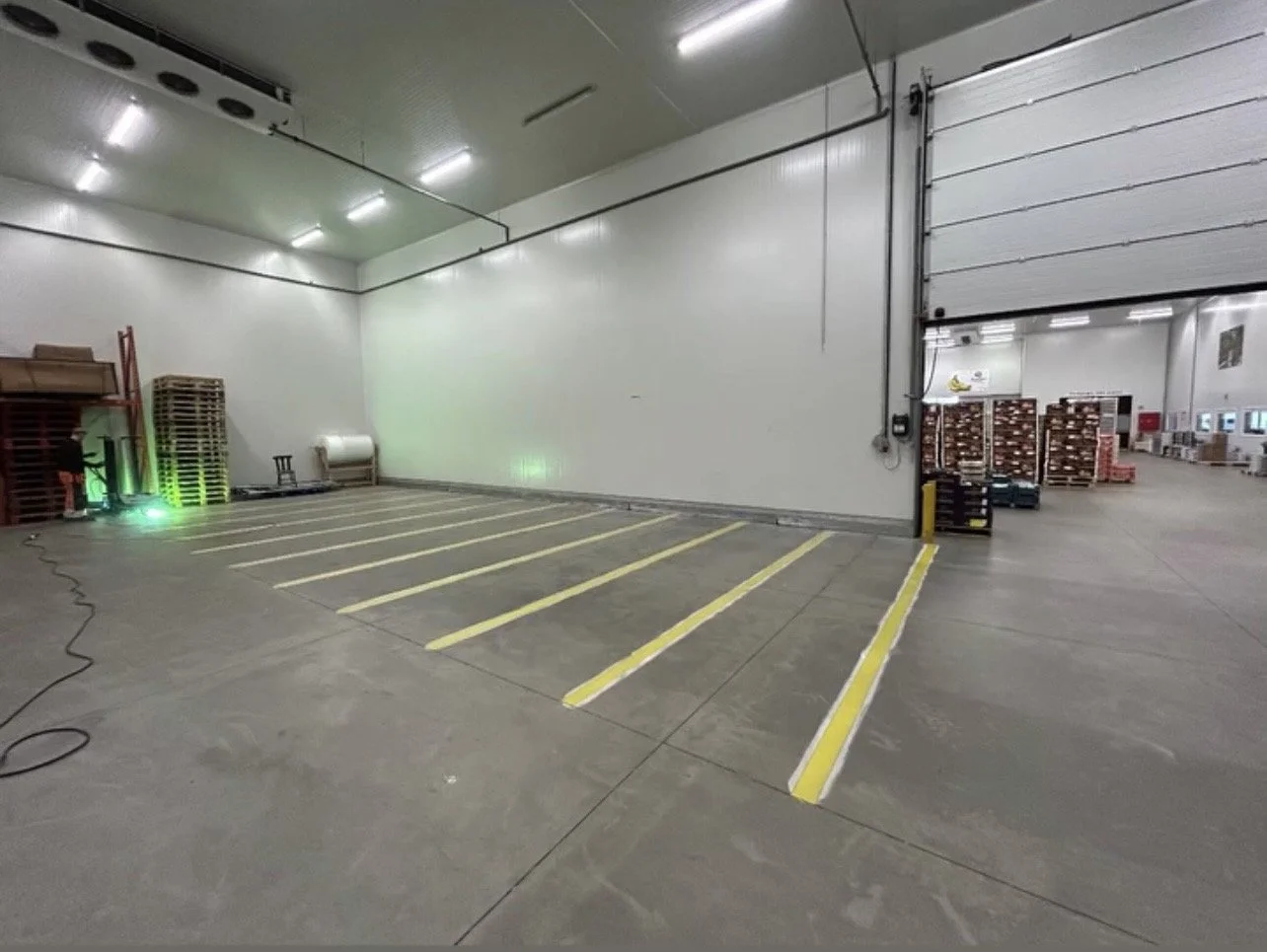 Lege parkeerplaatsen binnen een magazijn, scheidingslijnen in geel, pallets en magazijnmateriaal op de achtergrond.