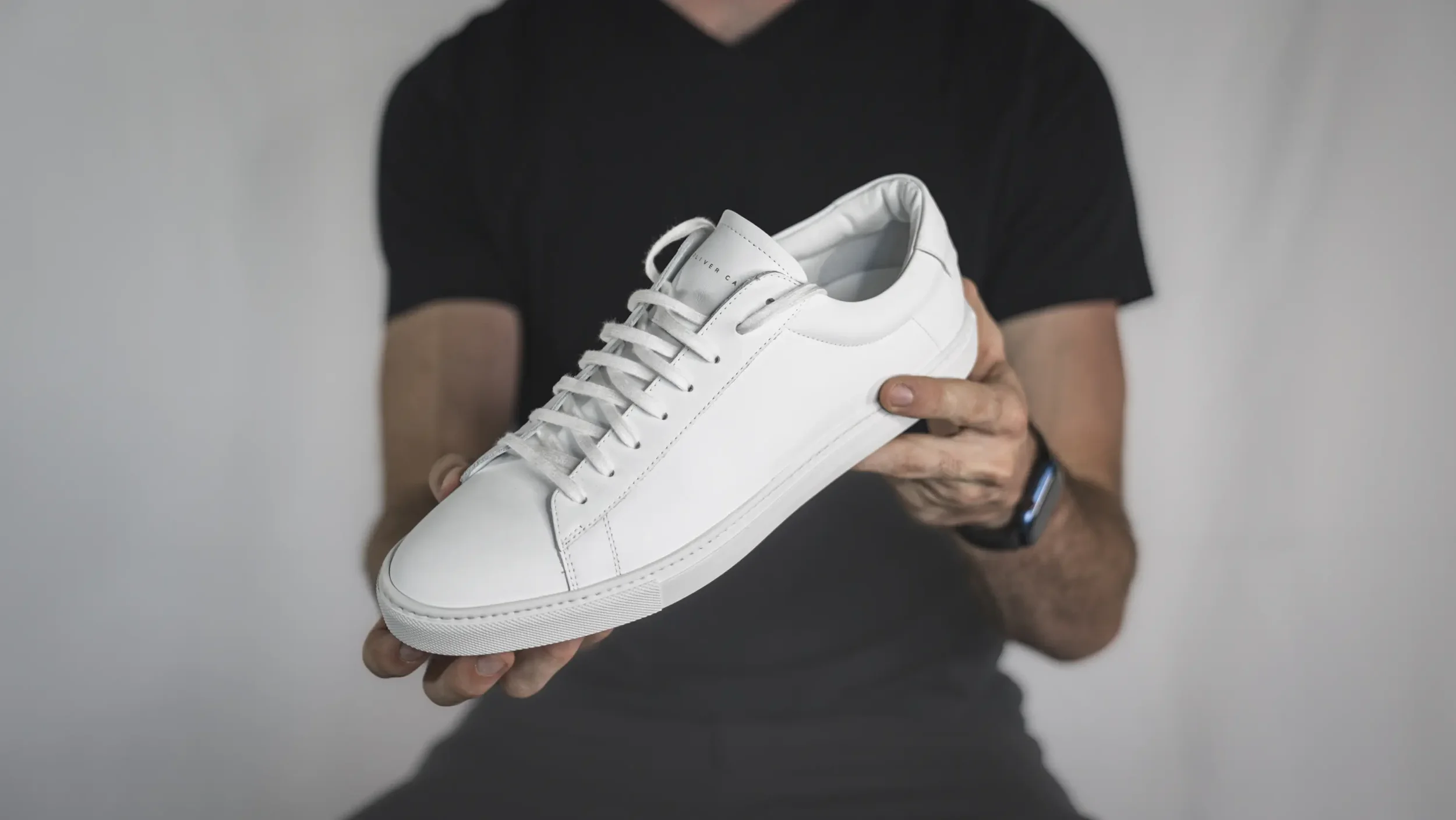 A person holding a white sneaker with both hands against a plain background.