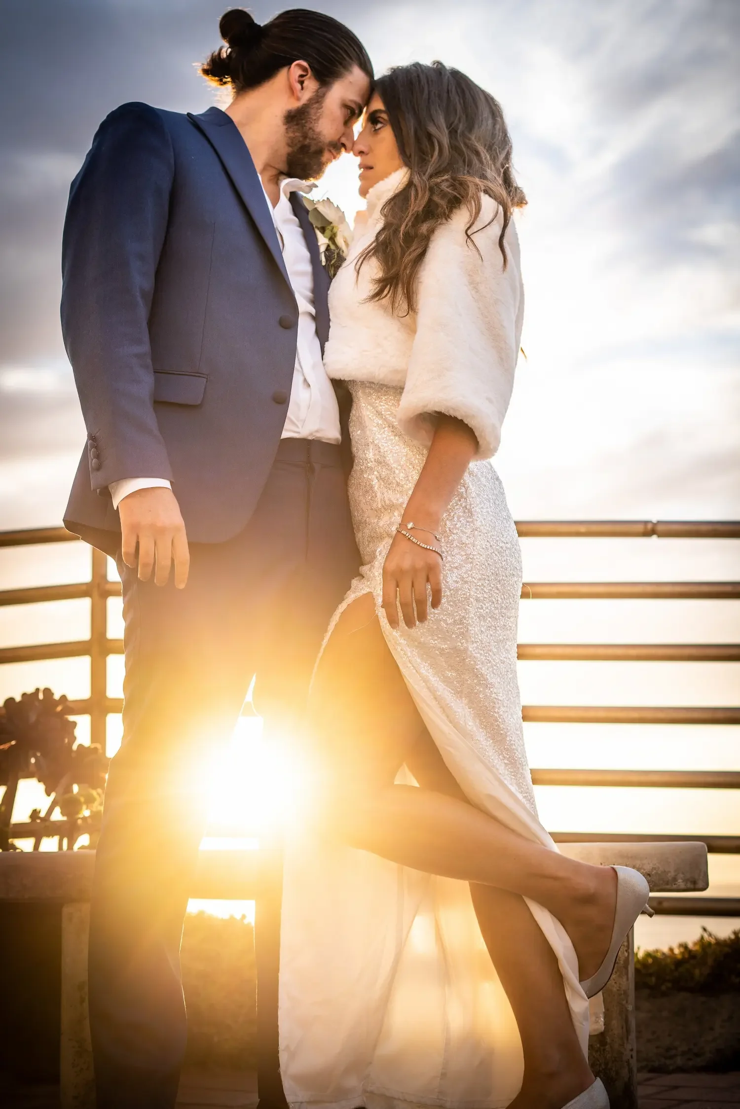 Bride and groom nose-to-nose at sunset, golden light flaring behind them