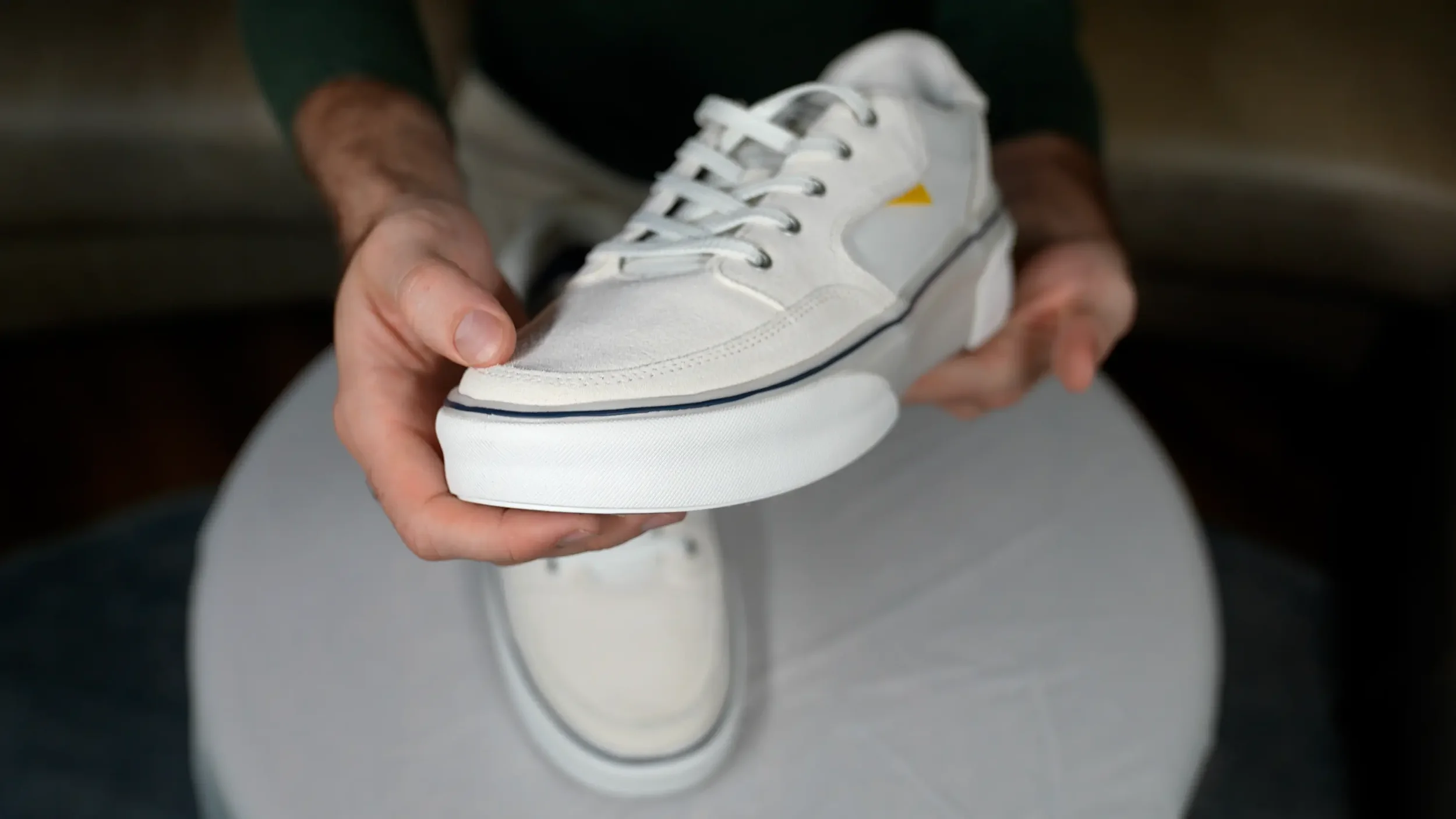 Person holding a white sneaker with gray and yellow accents.