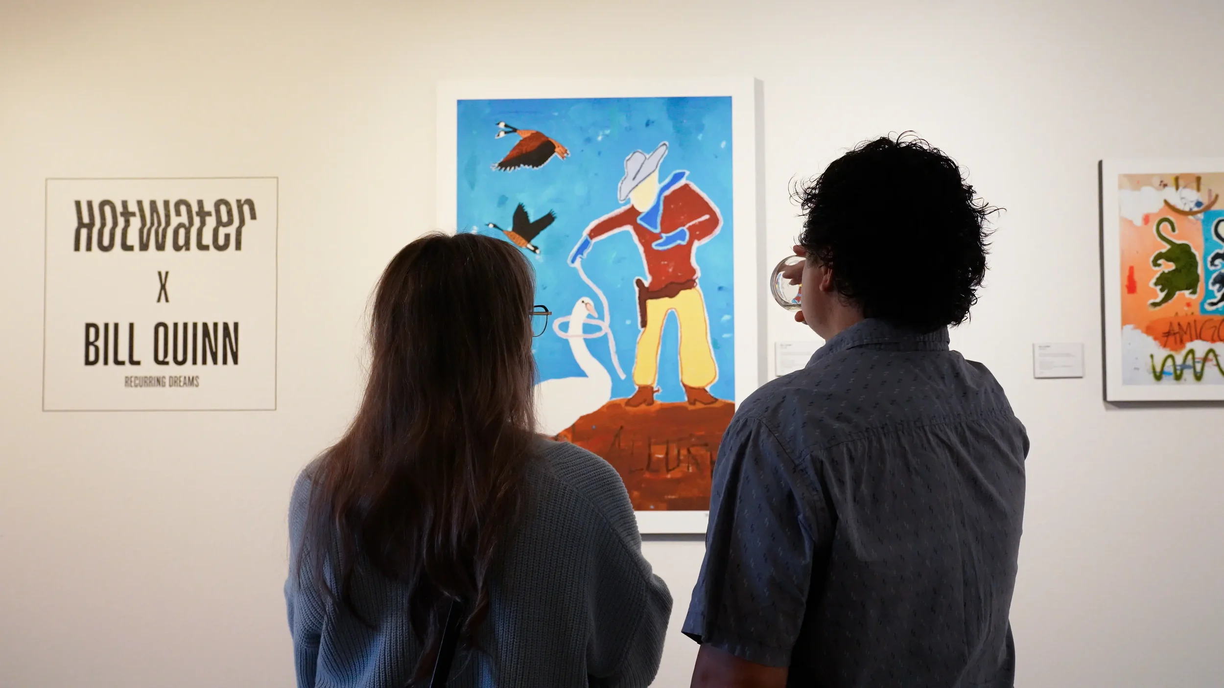 Two people viewing colorful artwork in an art gallery, with a poster on the wall that reads 'Hotwater x Bill Quinn Recurring Dreams'.