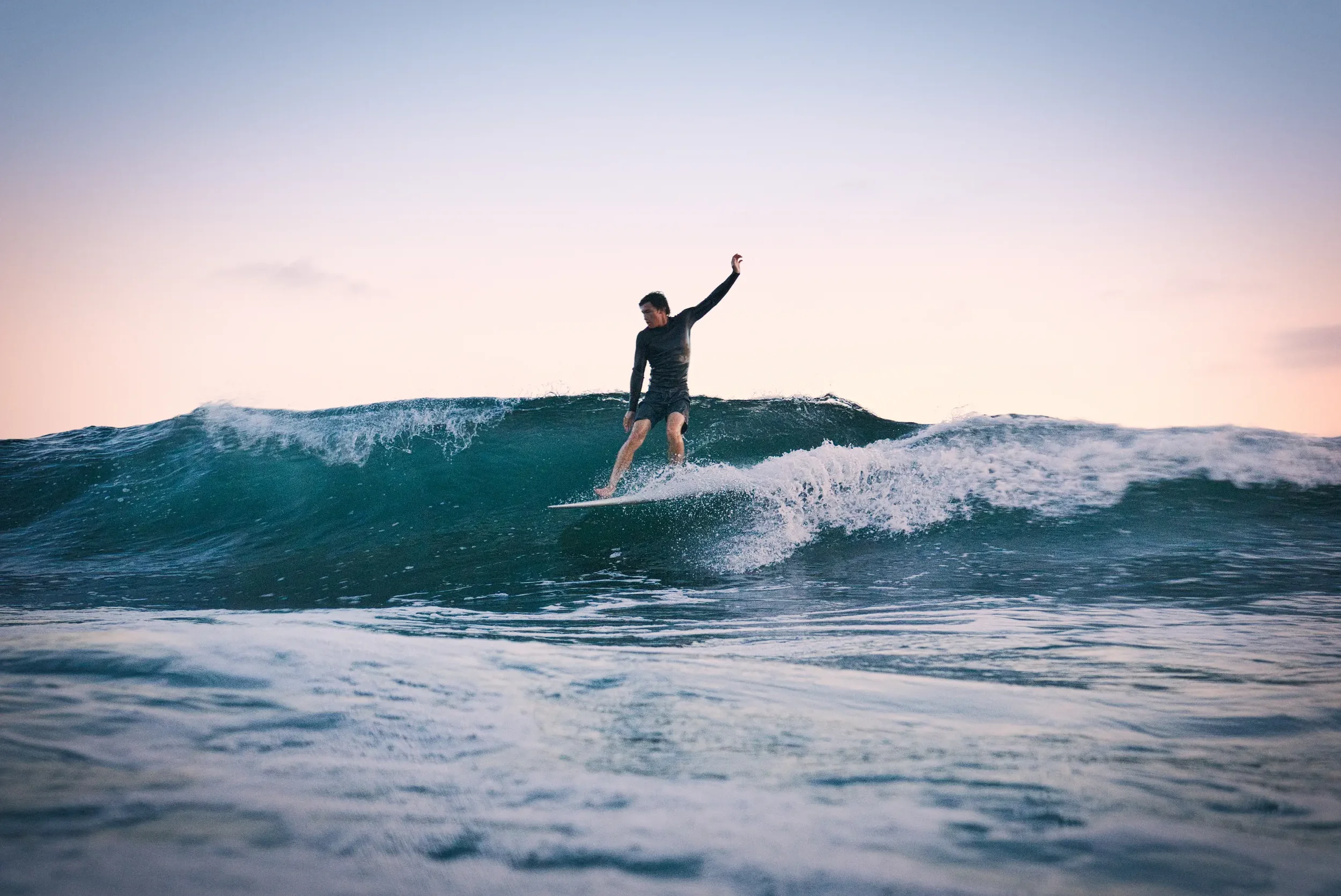 Person surfing on a wave during sunset or sunrise.