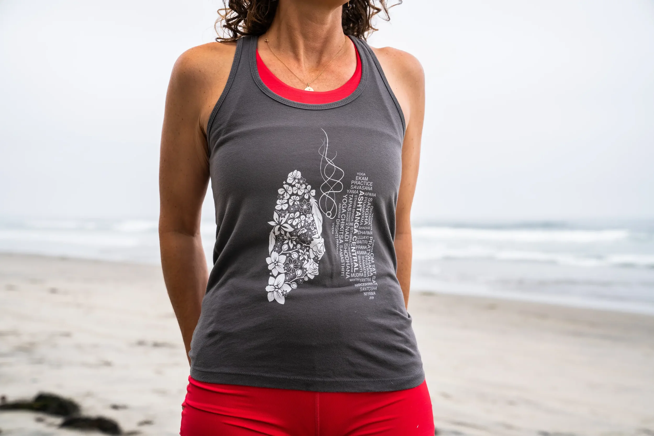 A woman in athletic clothing standing on a beach with the ocean in the background.