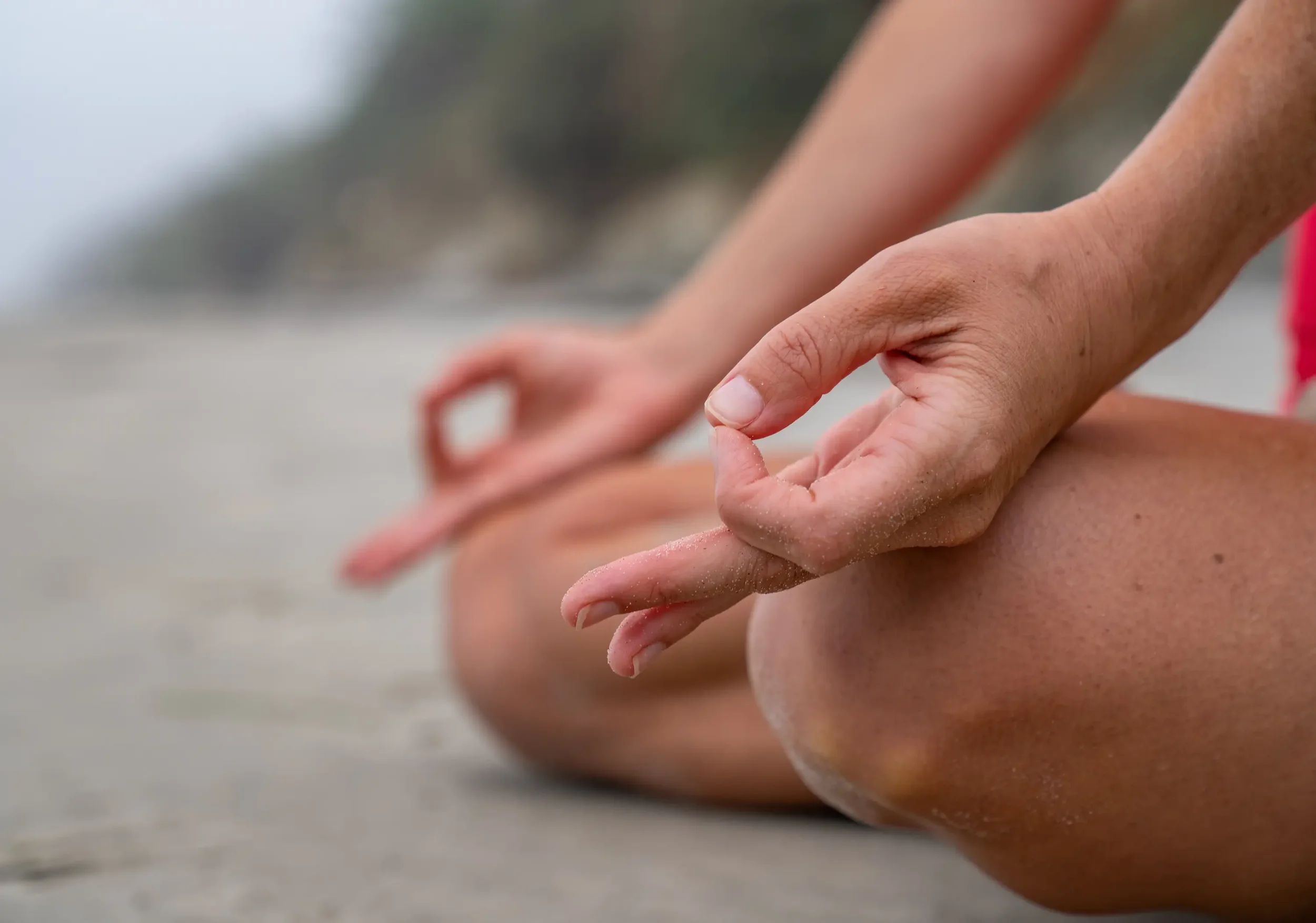 Close-up of people practicing yoga hands in a meditative pose on the beach.