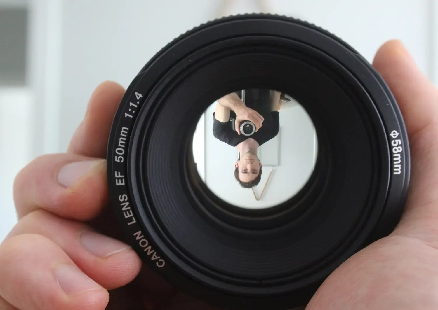 Close-up of a camera lens with the photographer's reflection visible inside, camera raised for the shot