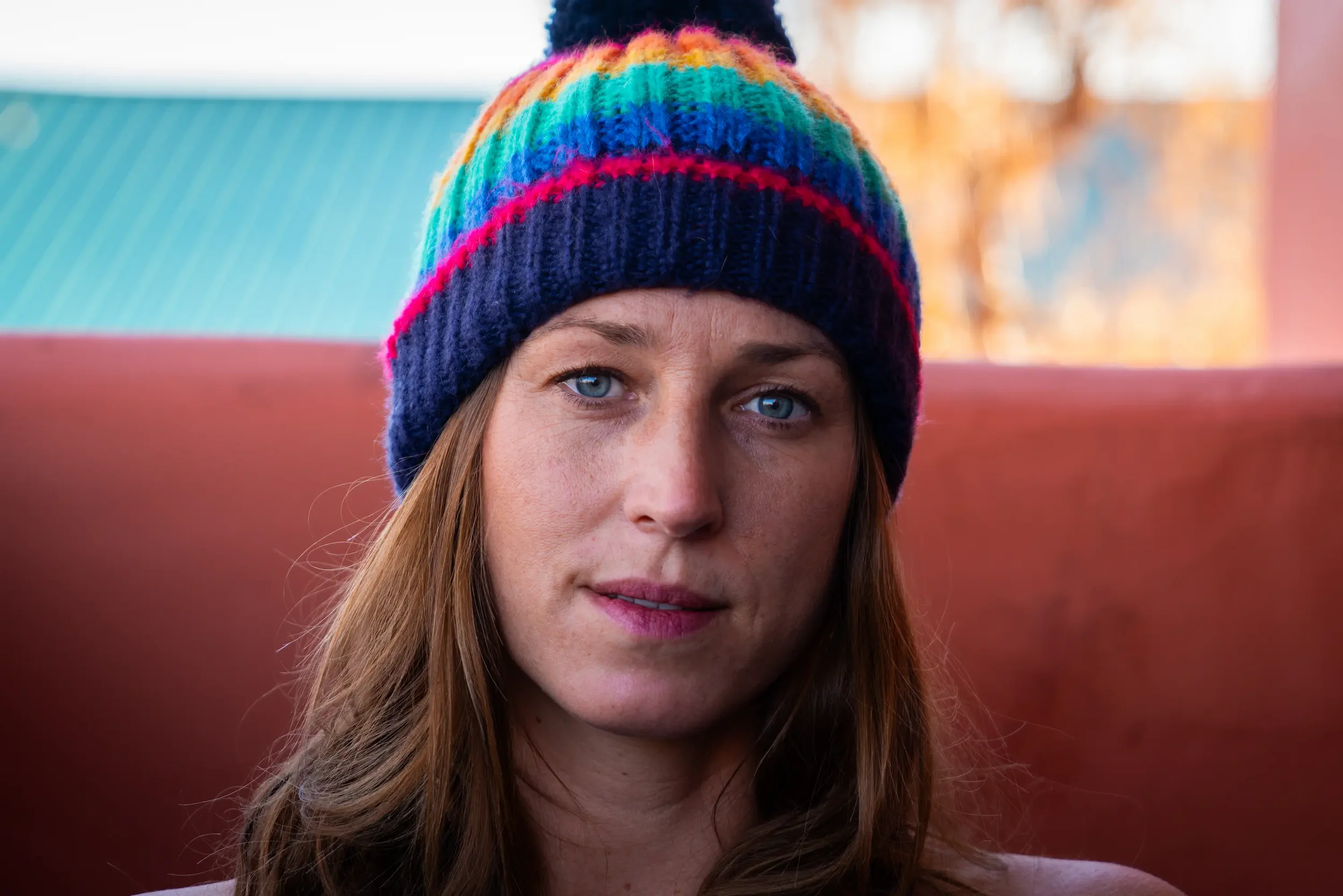 Close-up of a woman with red hair wearing a colorful rainbow striped knit beanie.